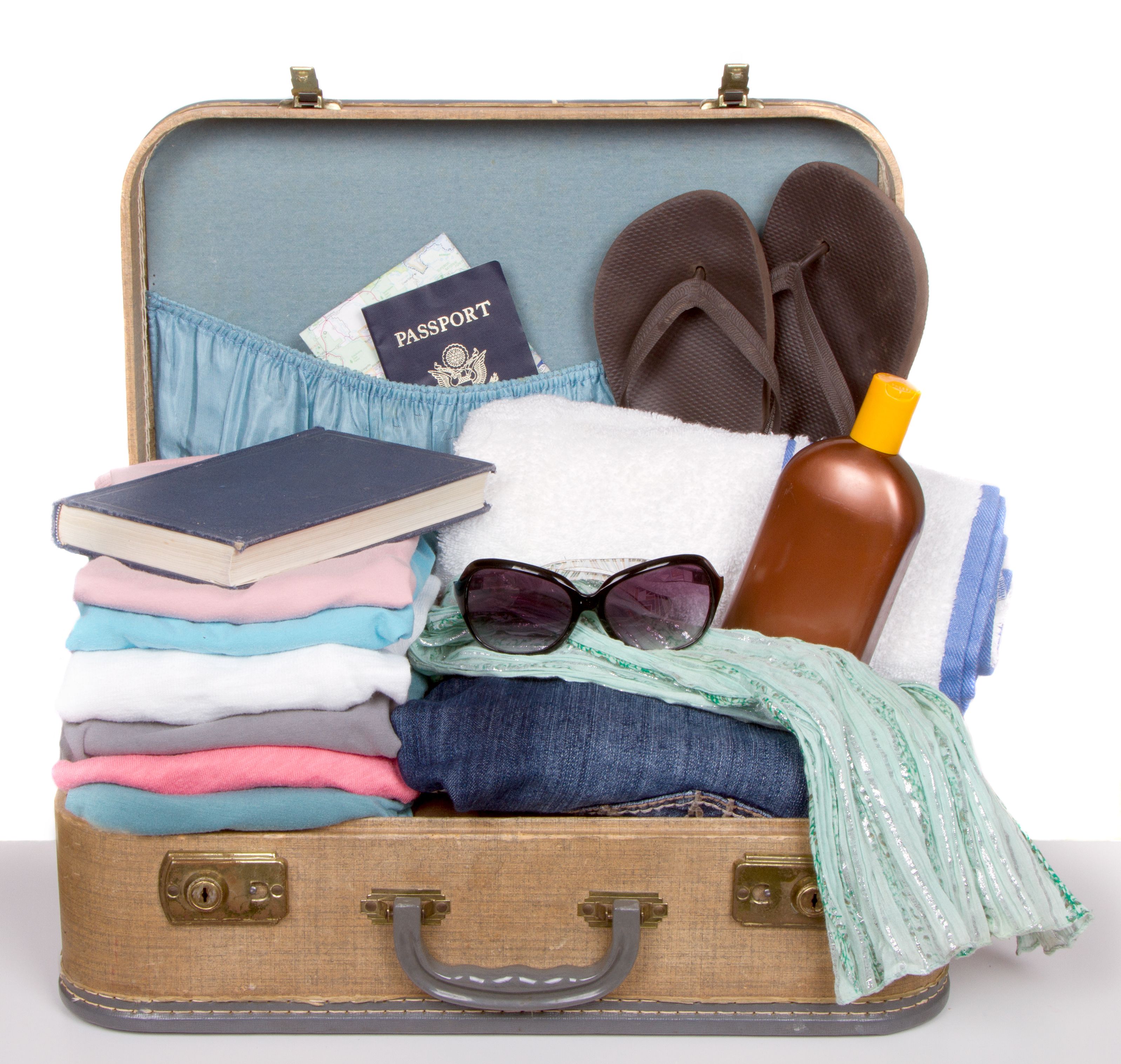 Vintage suitcase packed with travel necessities: colorful clothing, flip-flops, sunscreen, sunglasses, towel, and passport for a cruise vacation.