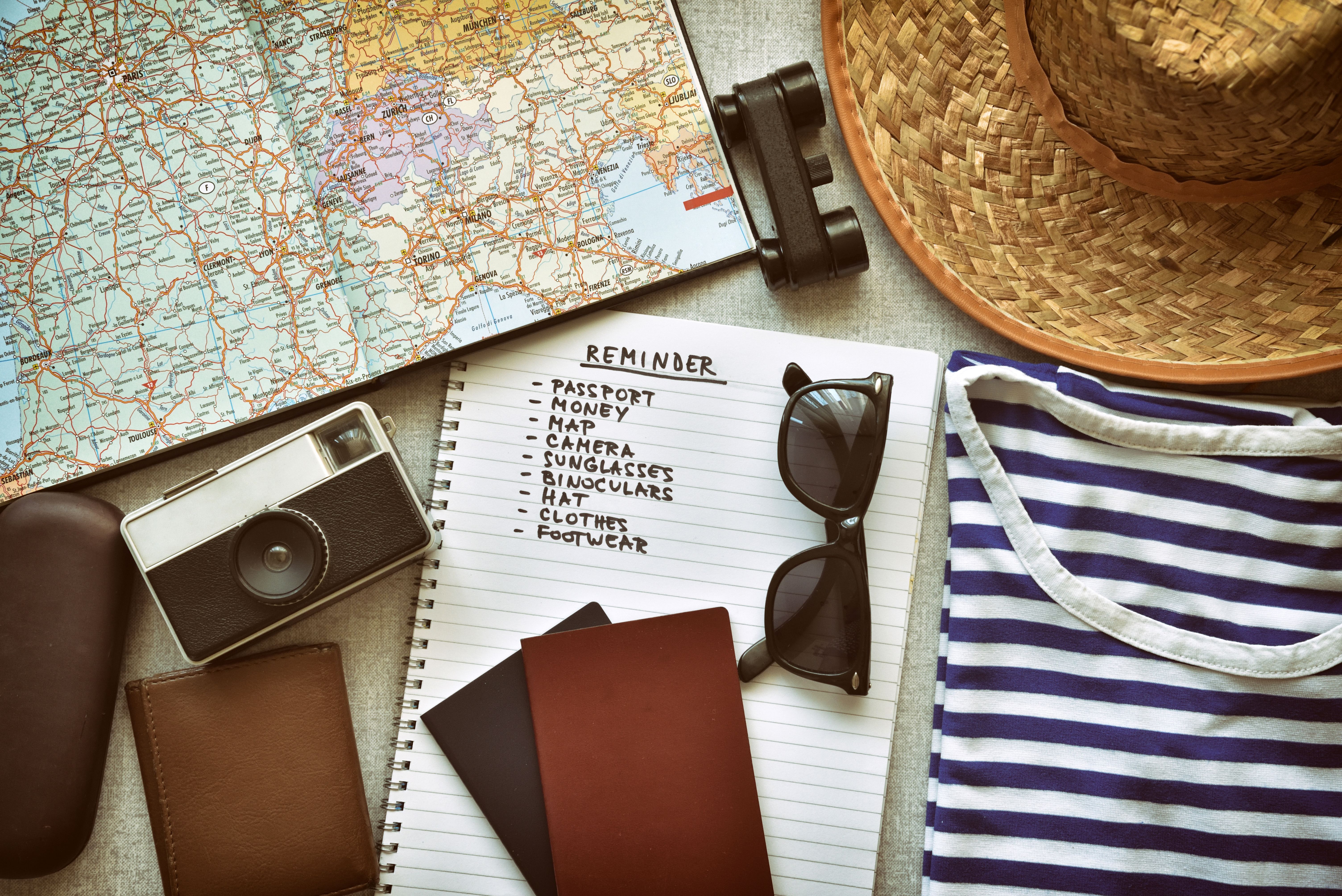 Cruise packing list with passport, wallet, vintage camera, binoculars, hat, sunglasses, and striped shirt on a map background.