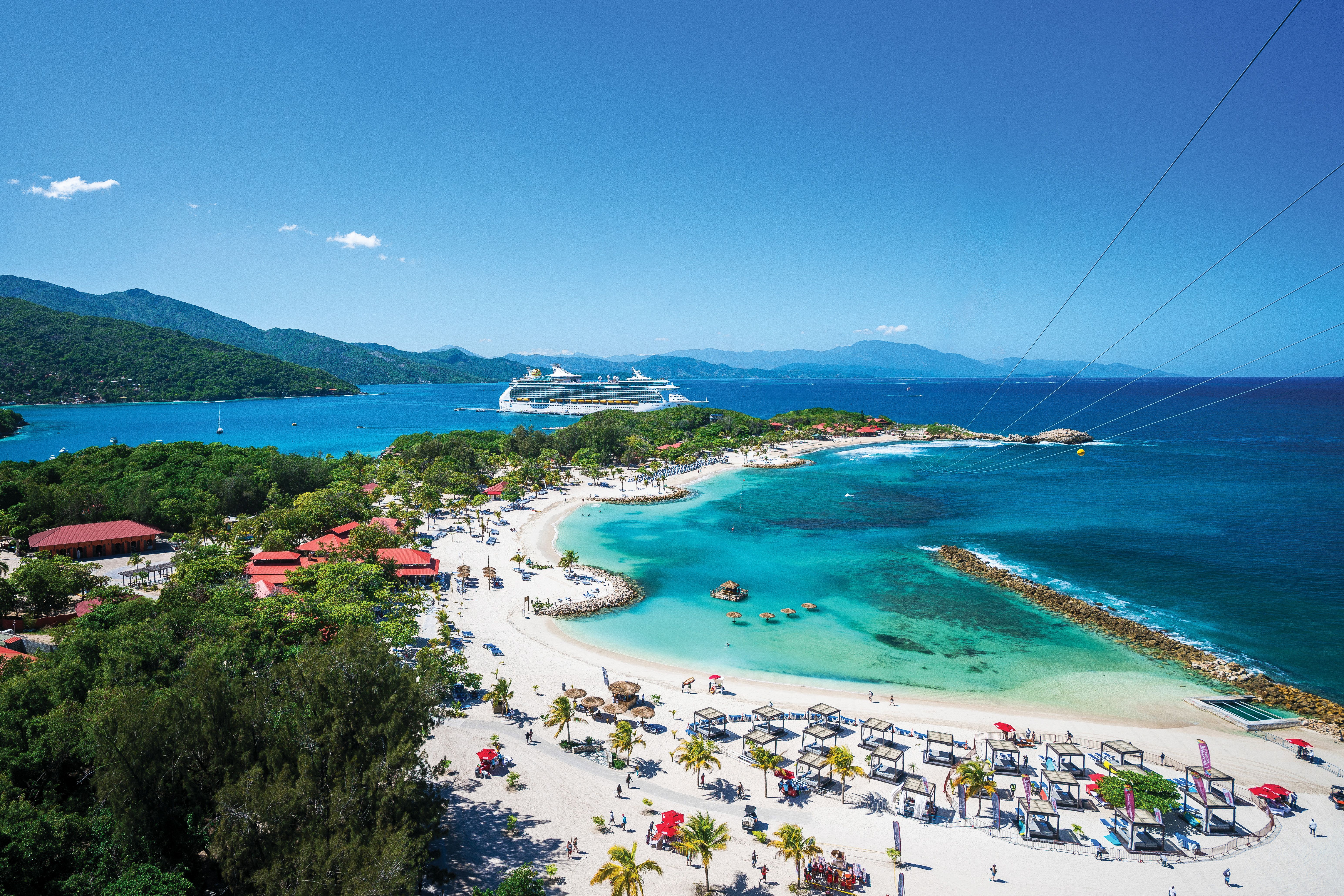 Aerial view of Labadee resort with guests on the beach and Royal Caribbean International cruise ship anchored offshore.