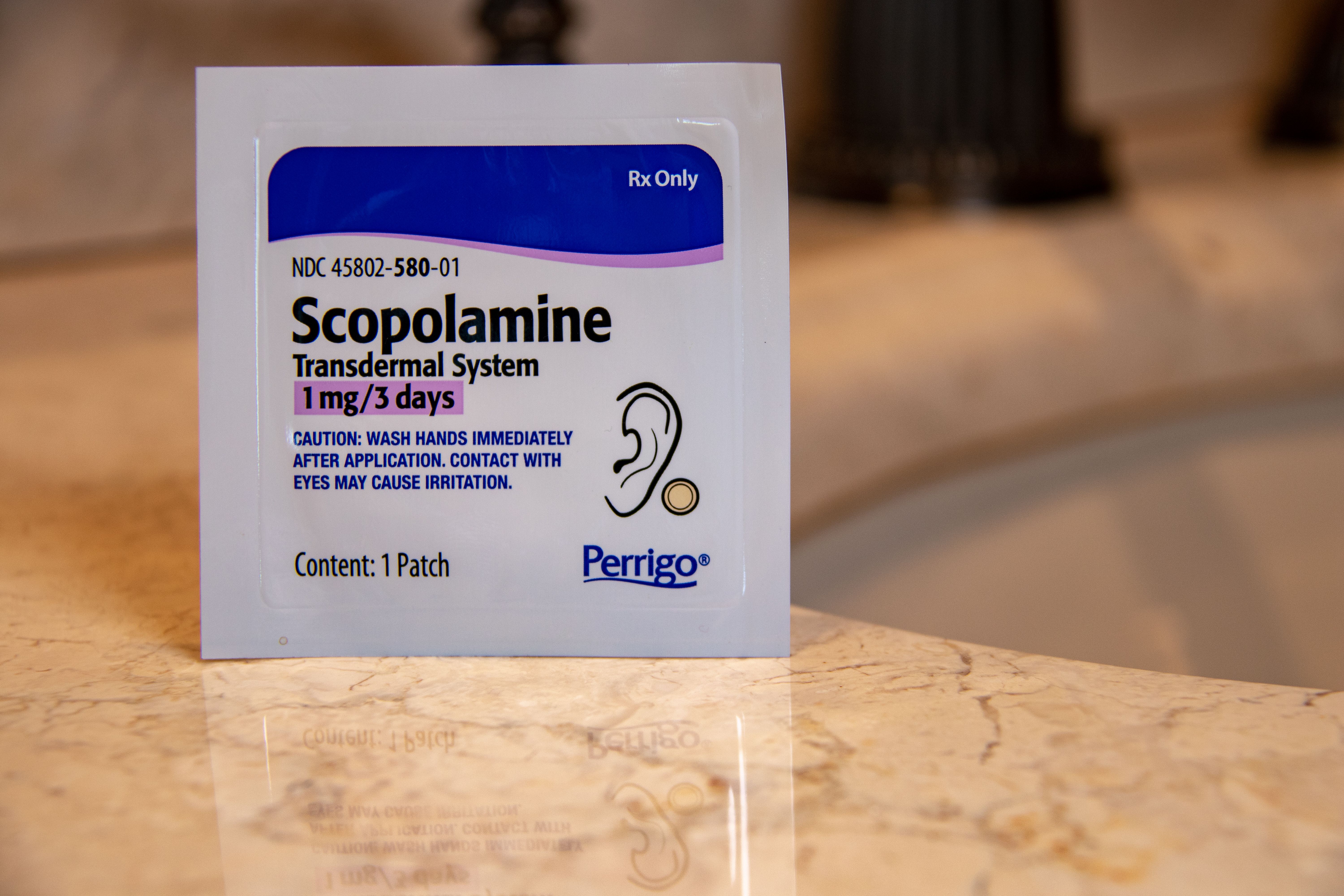 Scopolamine transdermal patch packaging on marble surface, a 3-day solution for cruise motion sickness prevention.