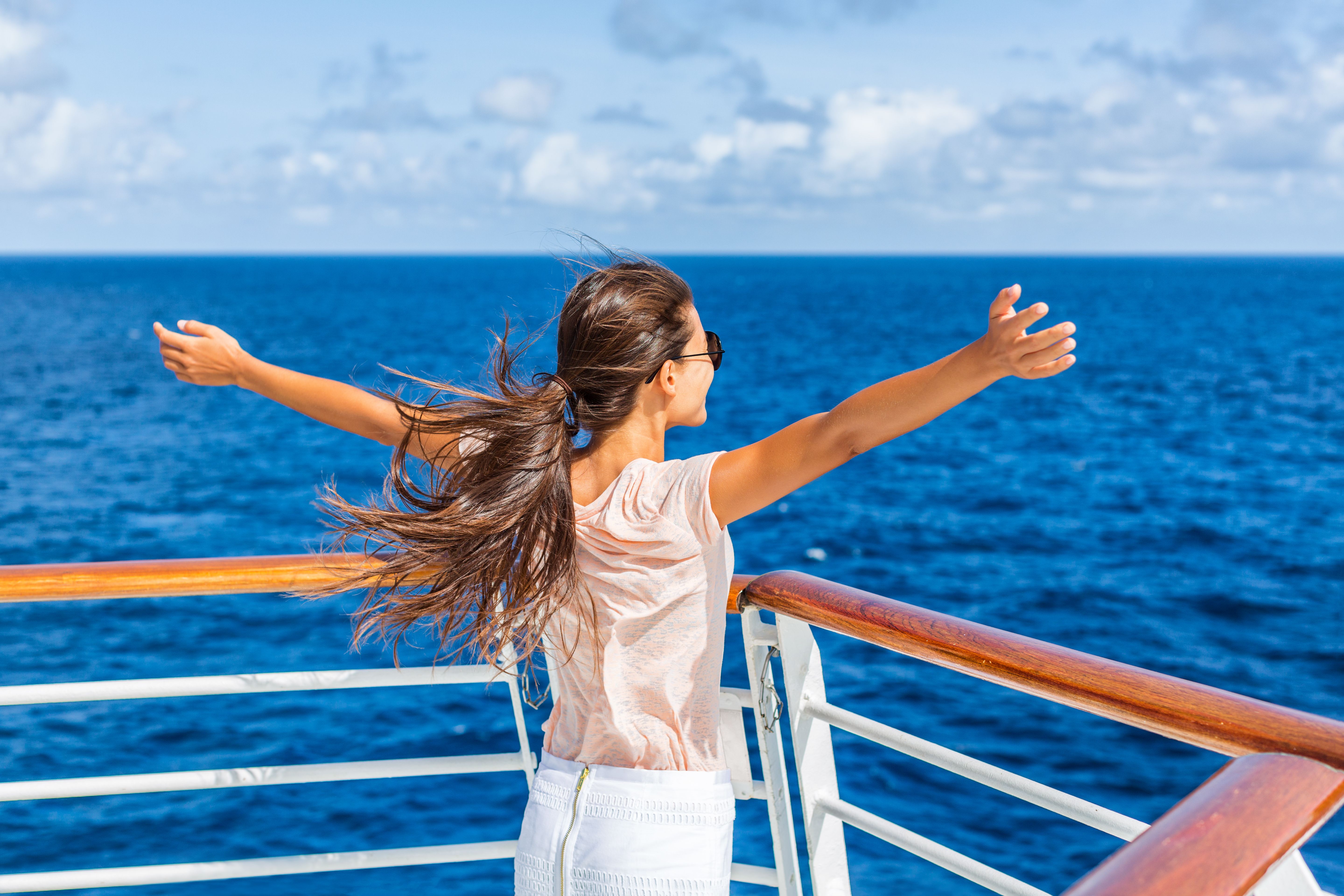 Woman with arms outstretched enjoying the sea breeze on a cruise ship deck, embodying joyful travel experiences.