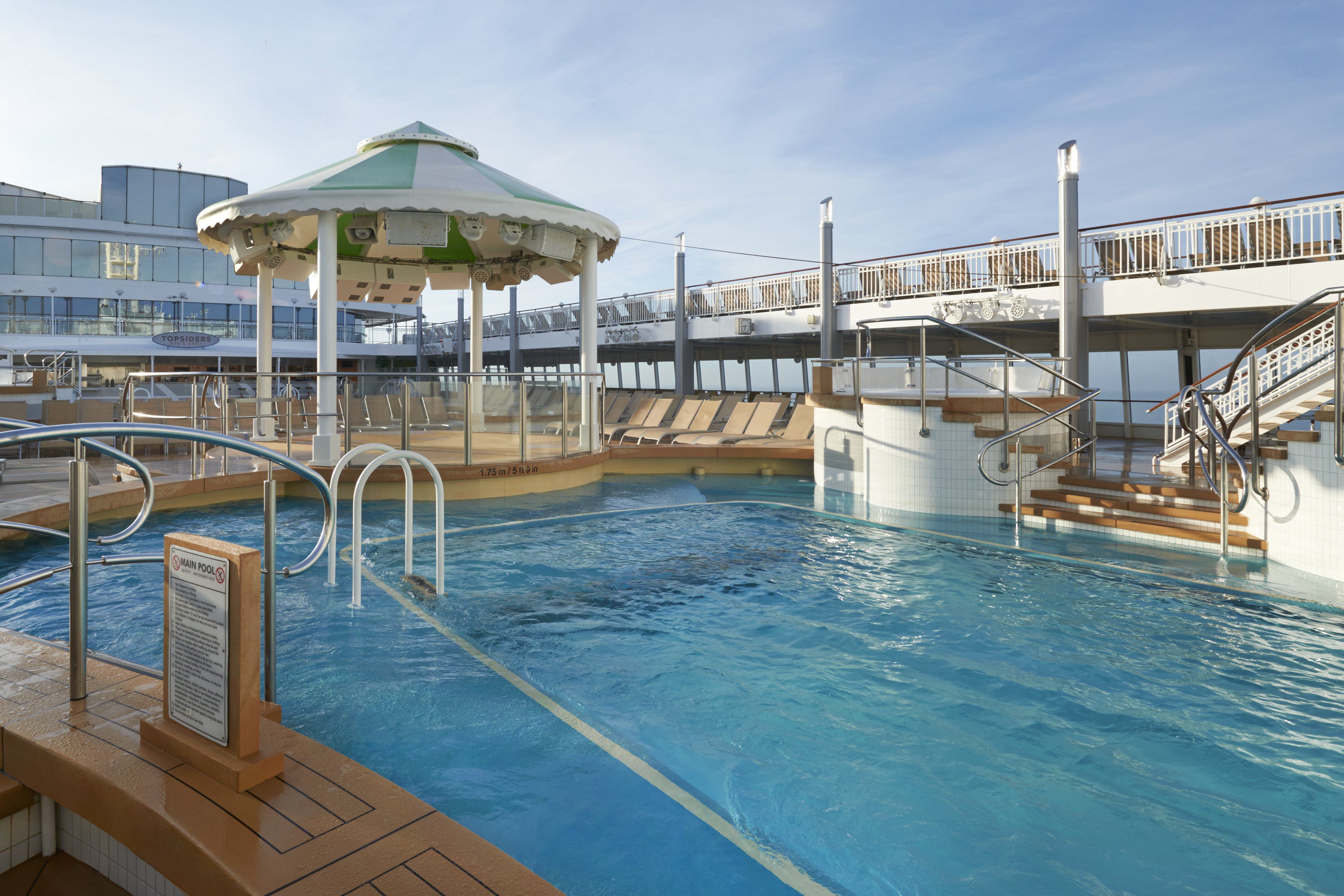 Tranquil NCL pool facility with a shaded bar area, sun loungers, and refreshing blue waters, perfect for a relaxing day at sea.