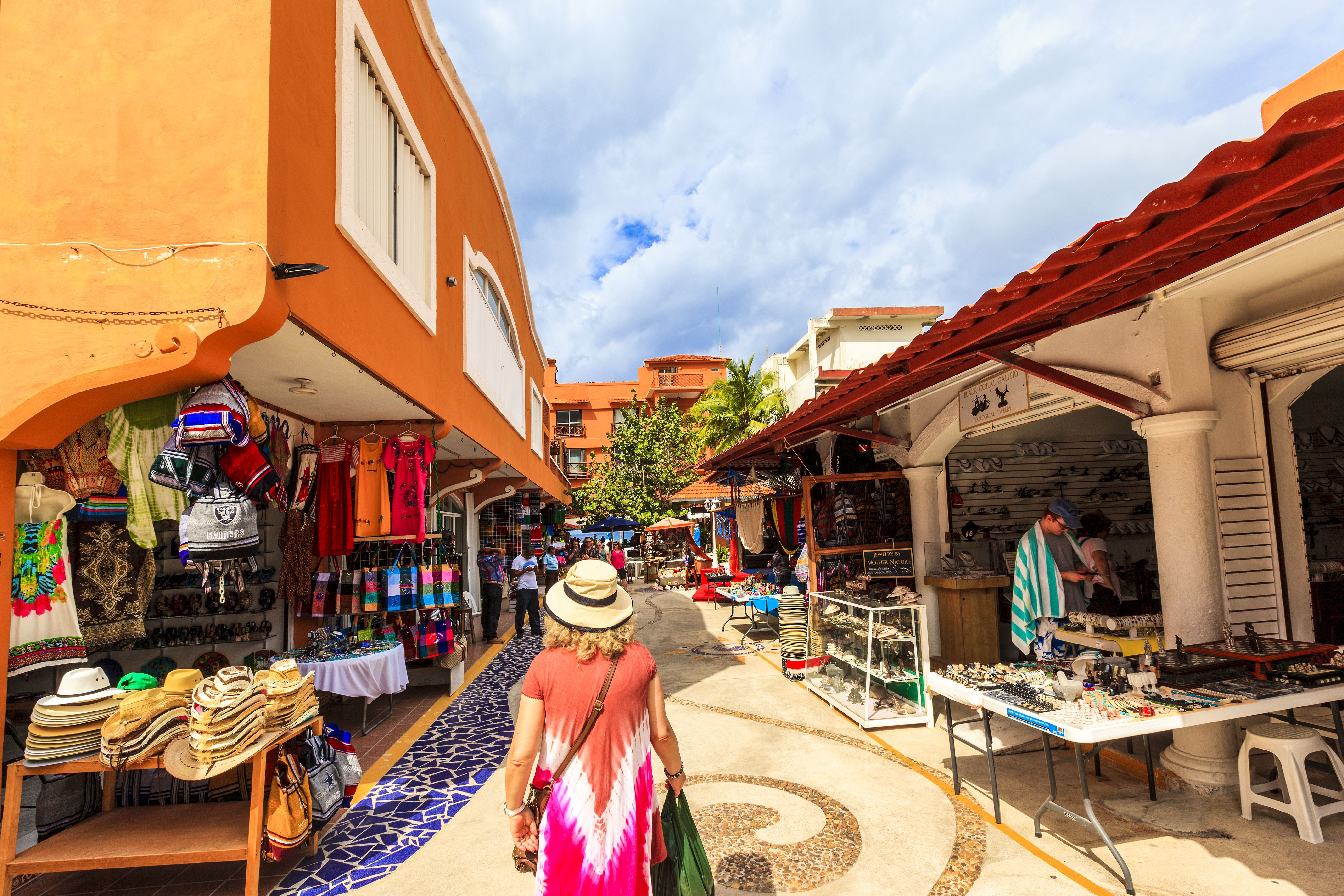 Guests of Oceania Cruises enjoy local shopping in Cozumel, strolling through vibrant market stalls under a sunny sky, highlighting cultural experiences.