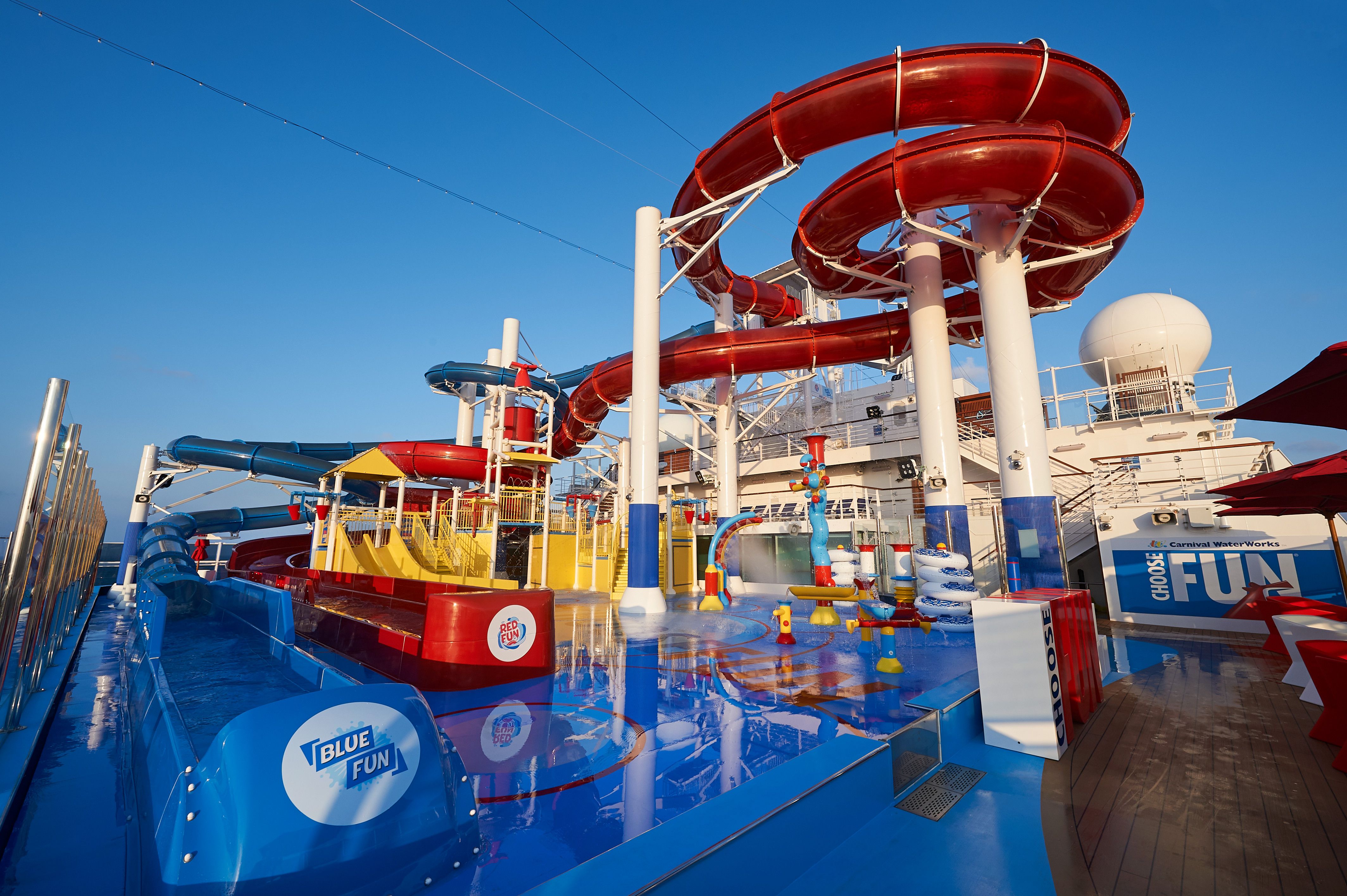 Carnival Panorama's WaterWorks with spiraling red slides and splash zone, clear skies above.