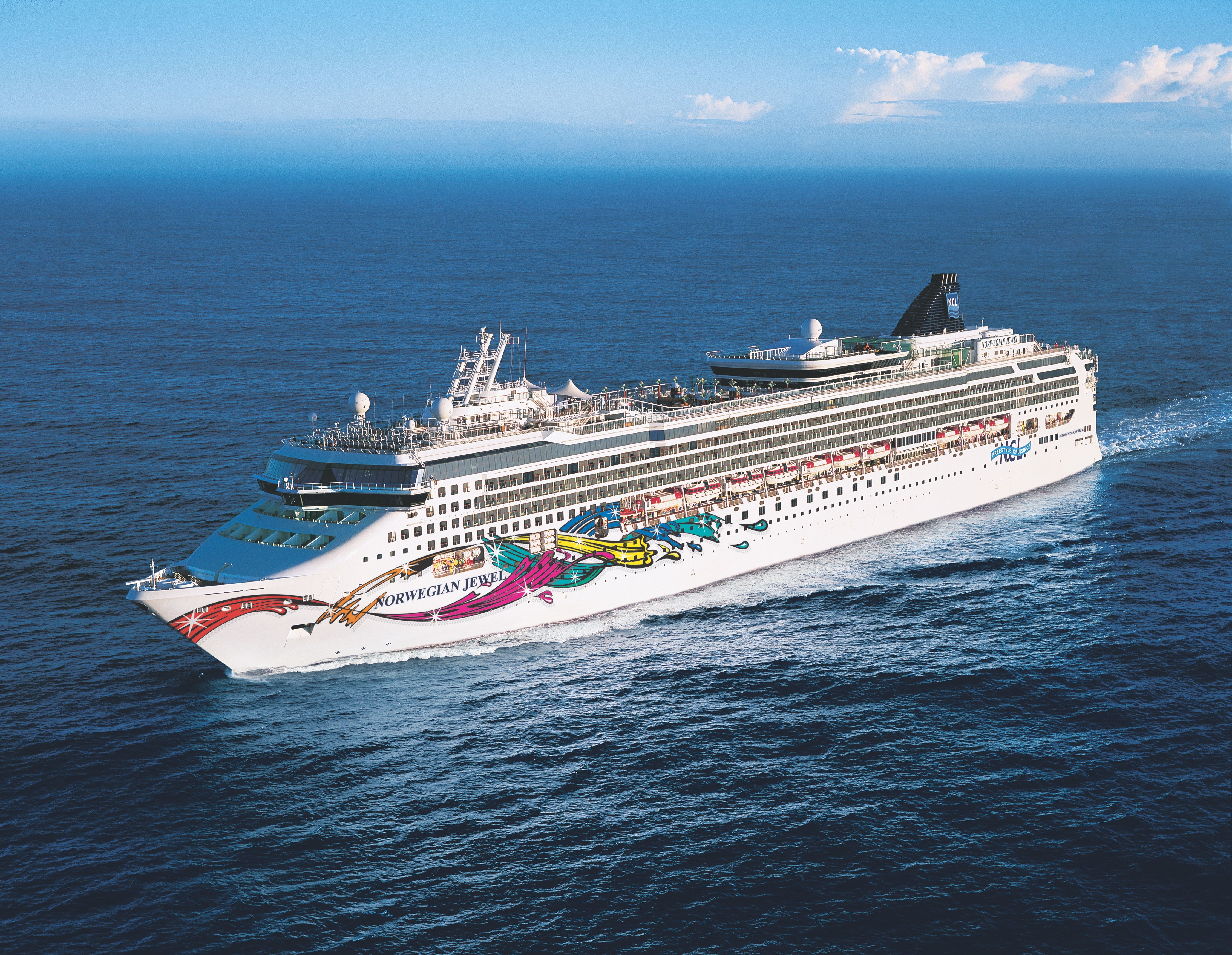 Norwegian Jewel cruise ship from Norwegian Cruise Line captured in a high-angle shot cruising the deep blue sea, showcasing its vibrant hull art.