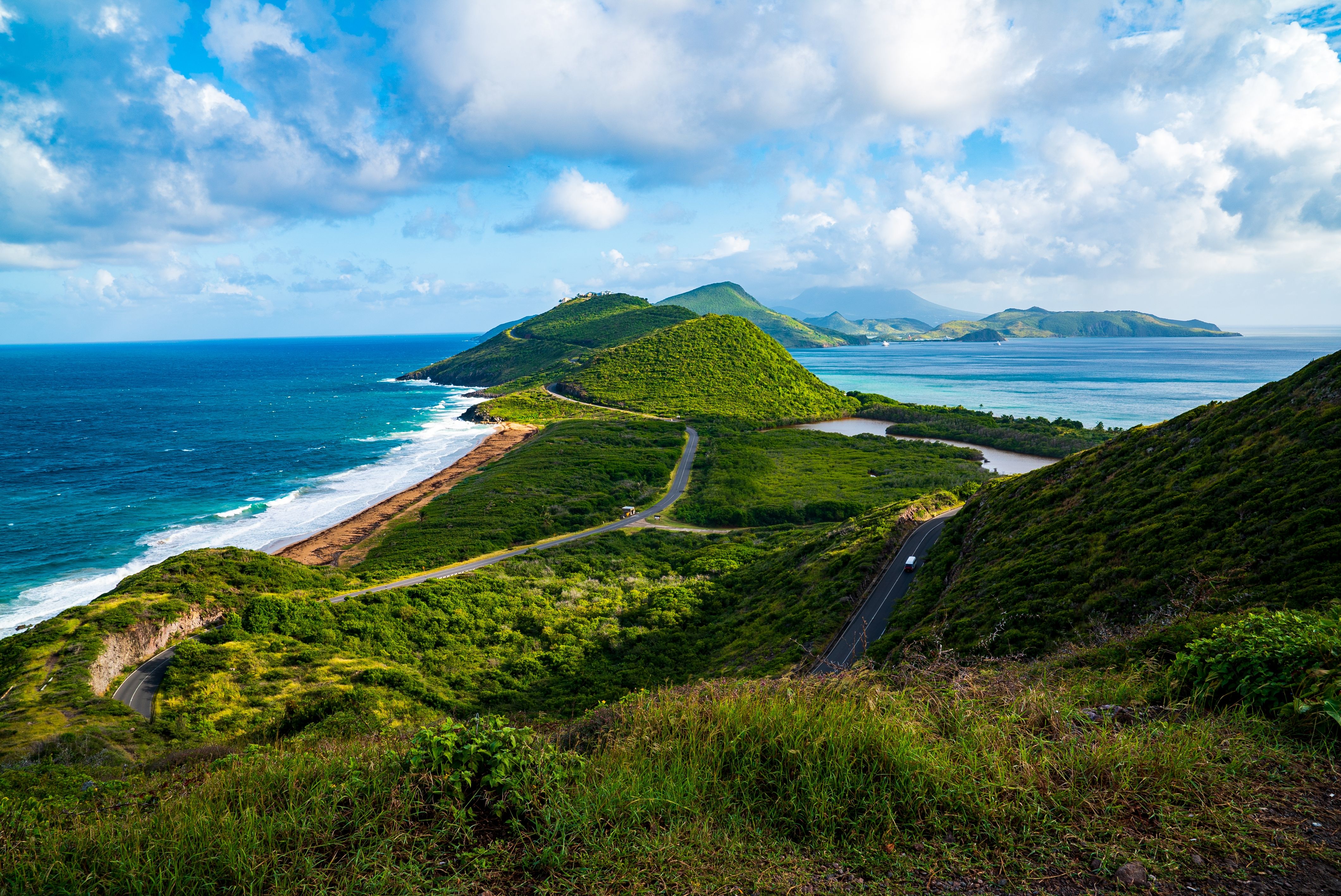 Lush, vibrant view of Cockleshell Beach in St. Kitts featuring winding roads along green hills and clear blue ocean waters.