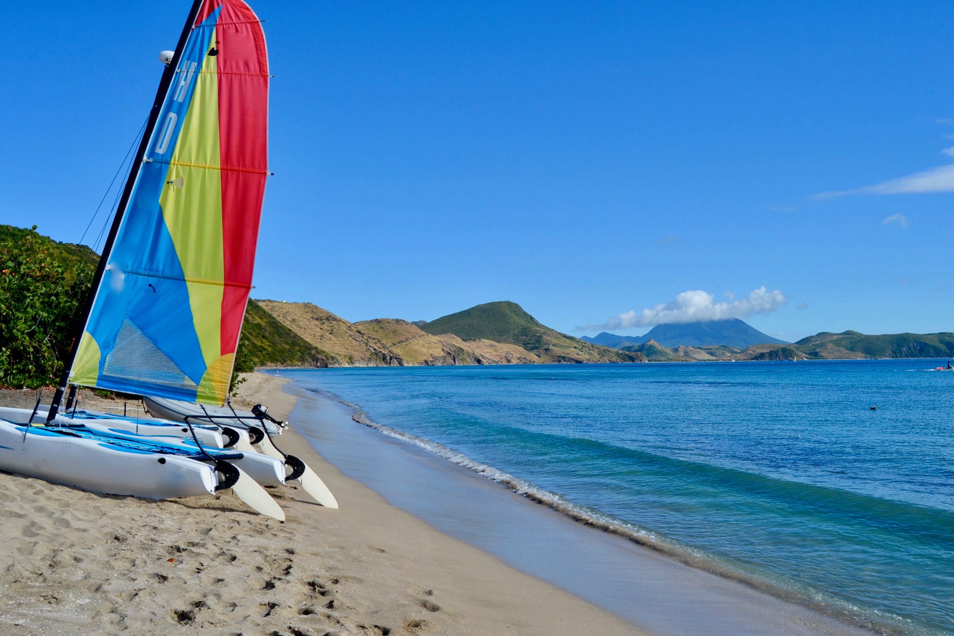 Colorful beach sailboat parked on sandy shores with blue ocean waters and green hills in the background.