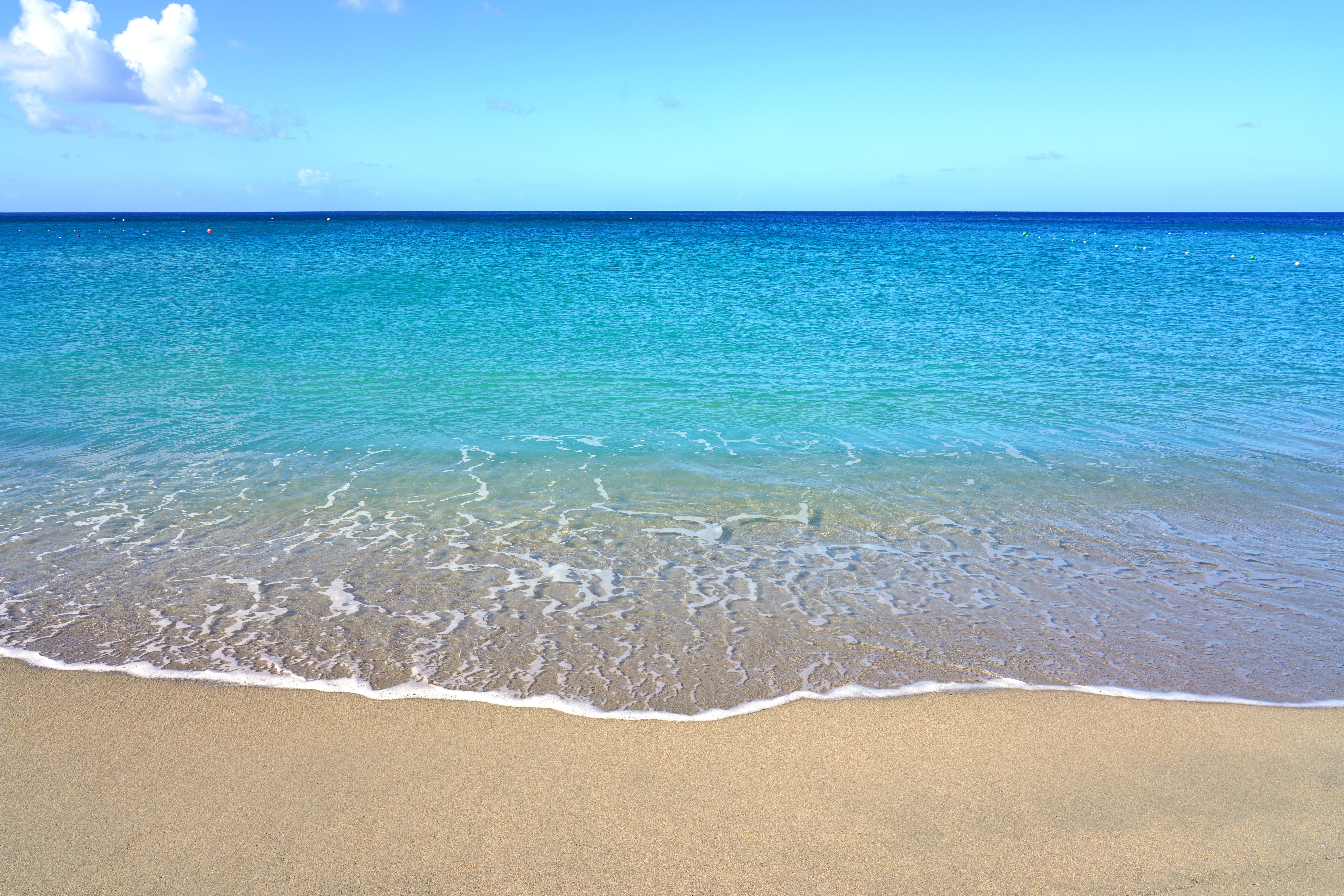 Clear turquoise waters and gentle waves at a tropical sandy beach with a deep blue horizon.