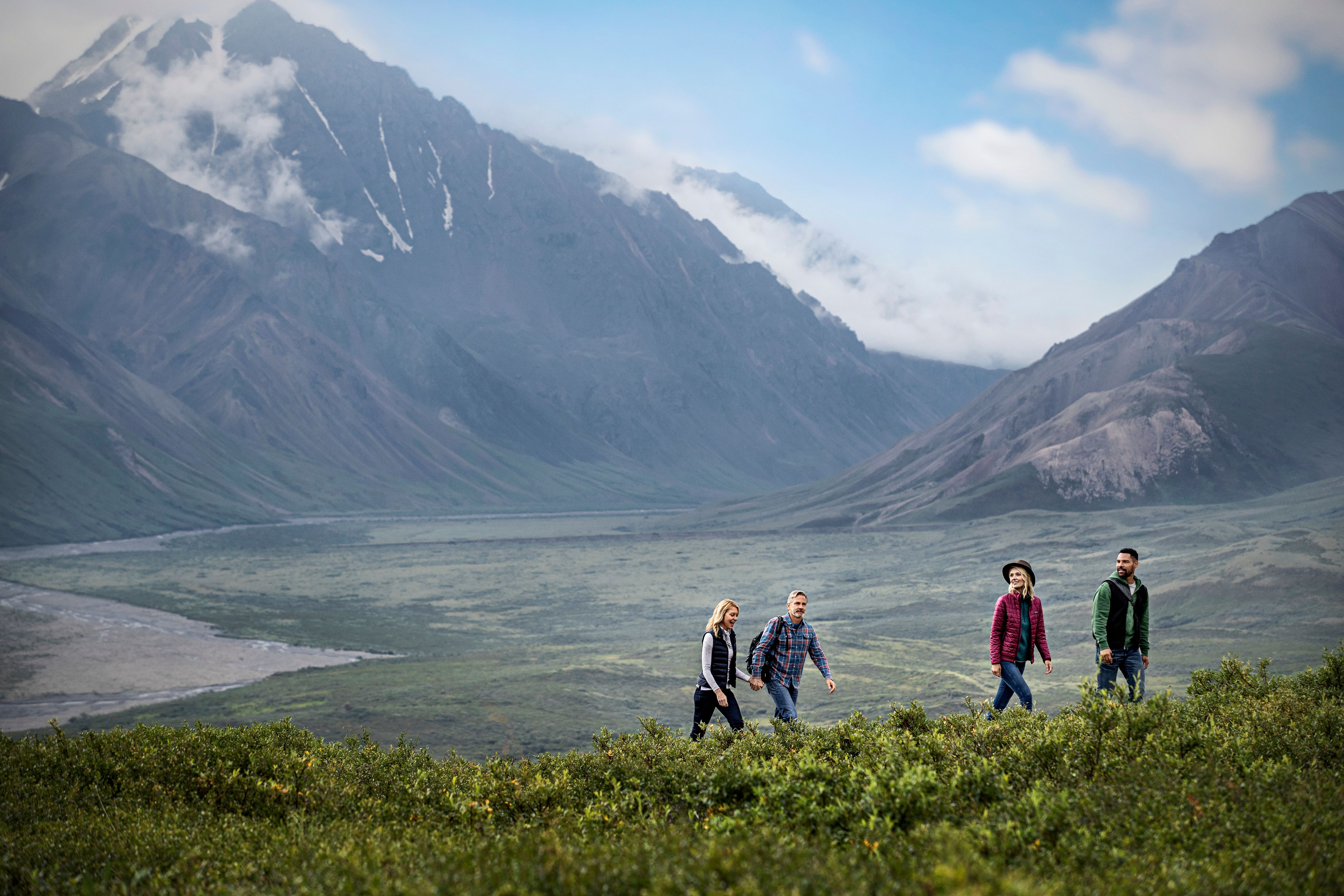 Group hiking through lush Alaskan valley with misty mountains.