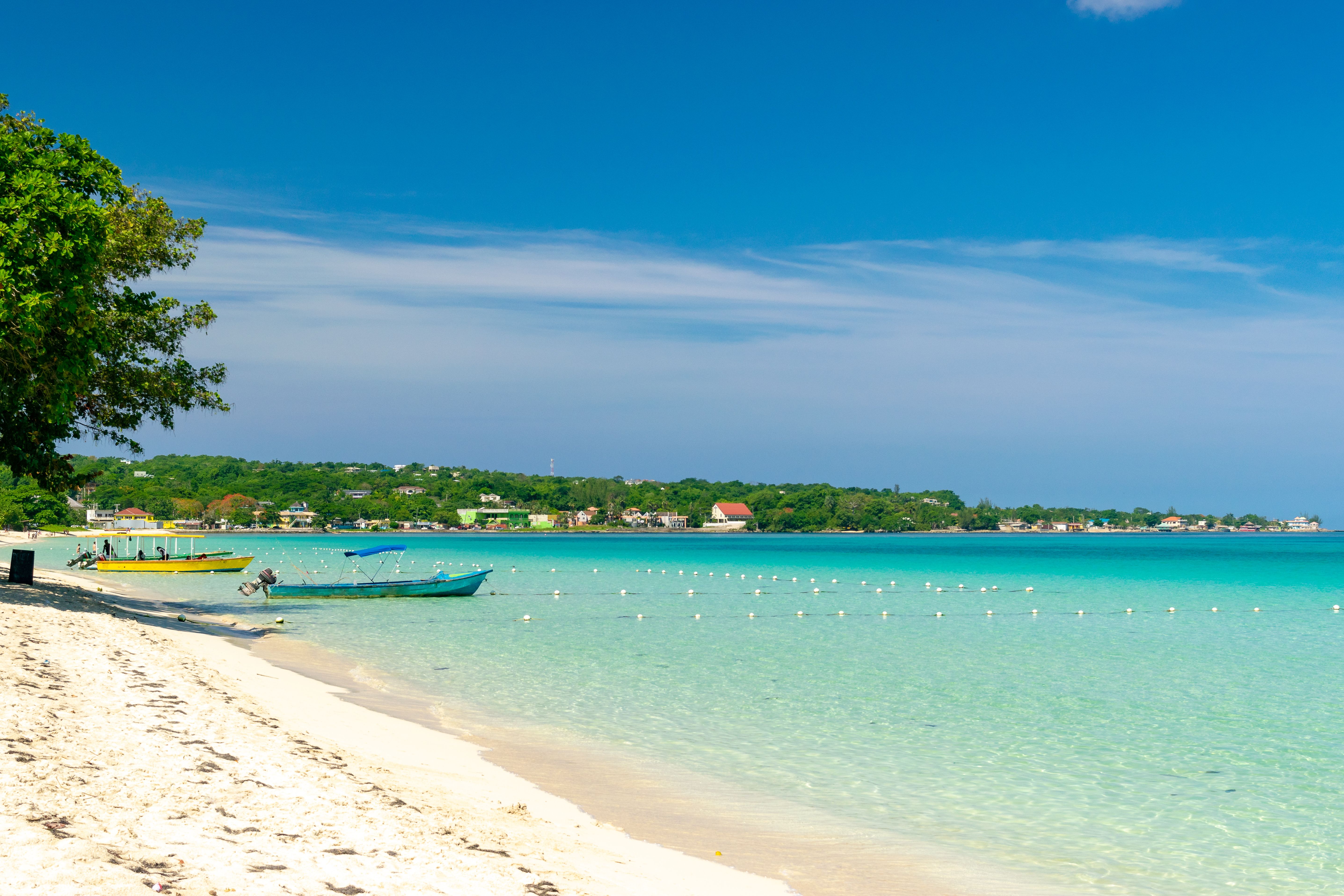 Pristine white sandy beach in Negril, Jamaica, with calm turquoise waters and anchored boats, a favorite cruise port of call.