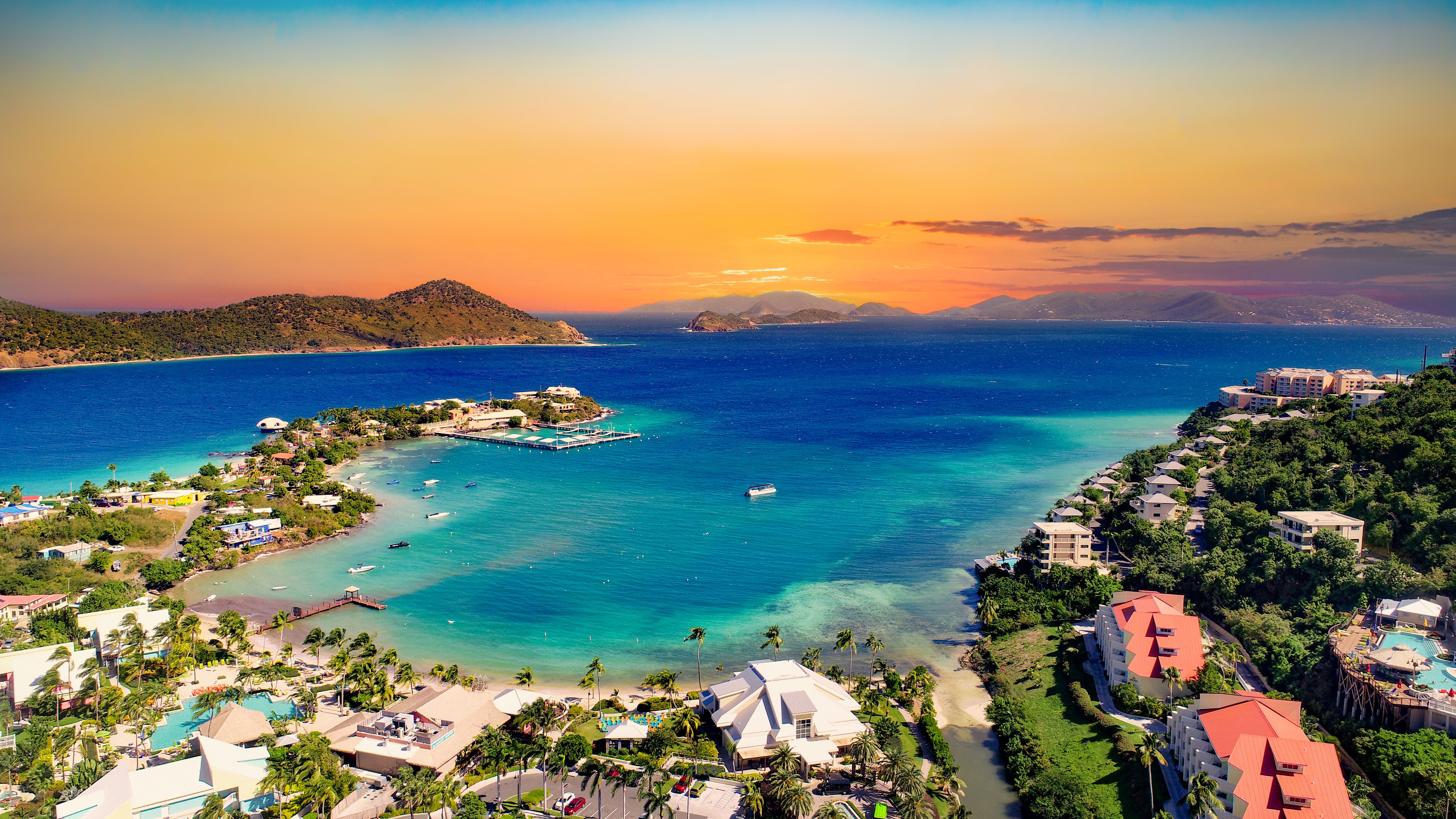 Vibrant sunset over the Caribbean Sea with lush hills, coastal resorts, and clear turquoise waters, a scenic cruise destination.