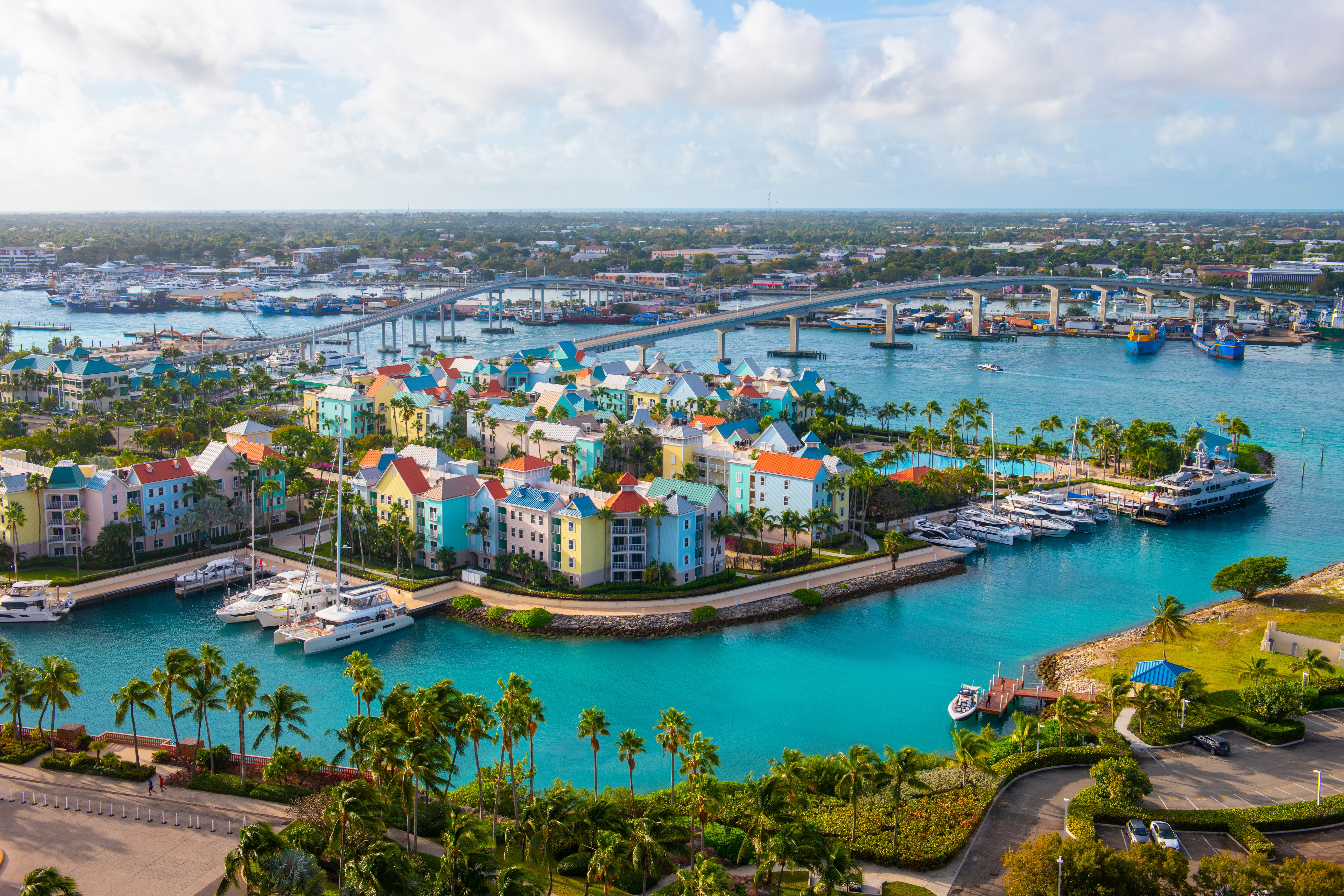 Colorful waterfront homes and marina in Nassau, Bahamas, with boats docked and a bridge in the background, popular cruise destination.