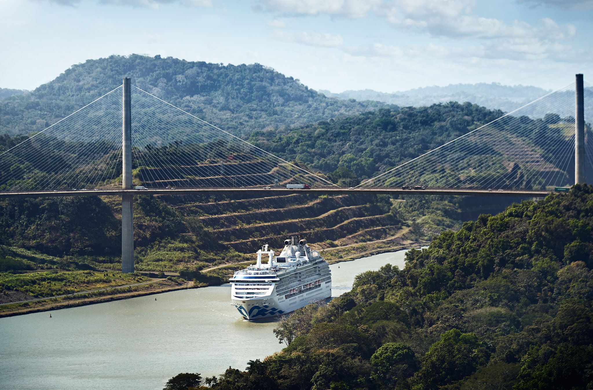 Cruise ship passing under the Centennial Bridge in the Panama Canal, surrounded by lush greenery, a scenic highlight of Princess Cruises.