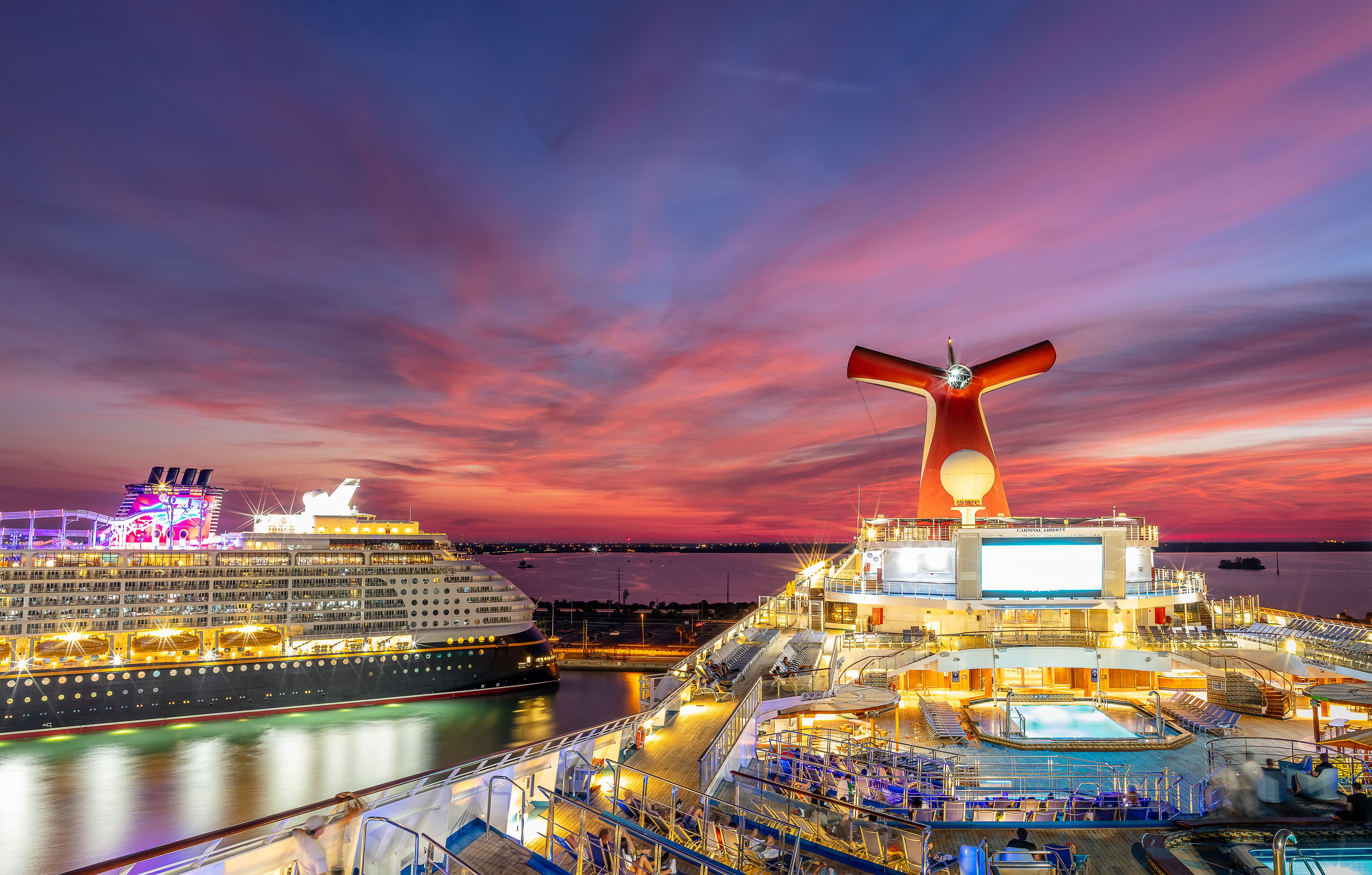 Carnival Cruise Line ship docked at Port Canaveral at sunset, with a vibrant sky and another cruise ship in the distance.