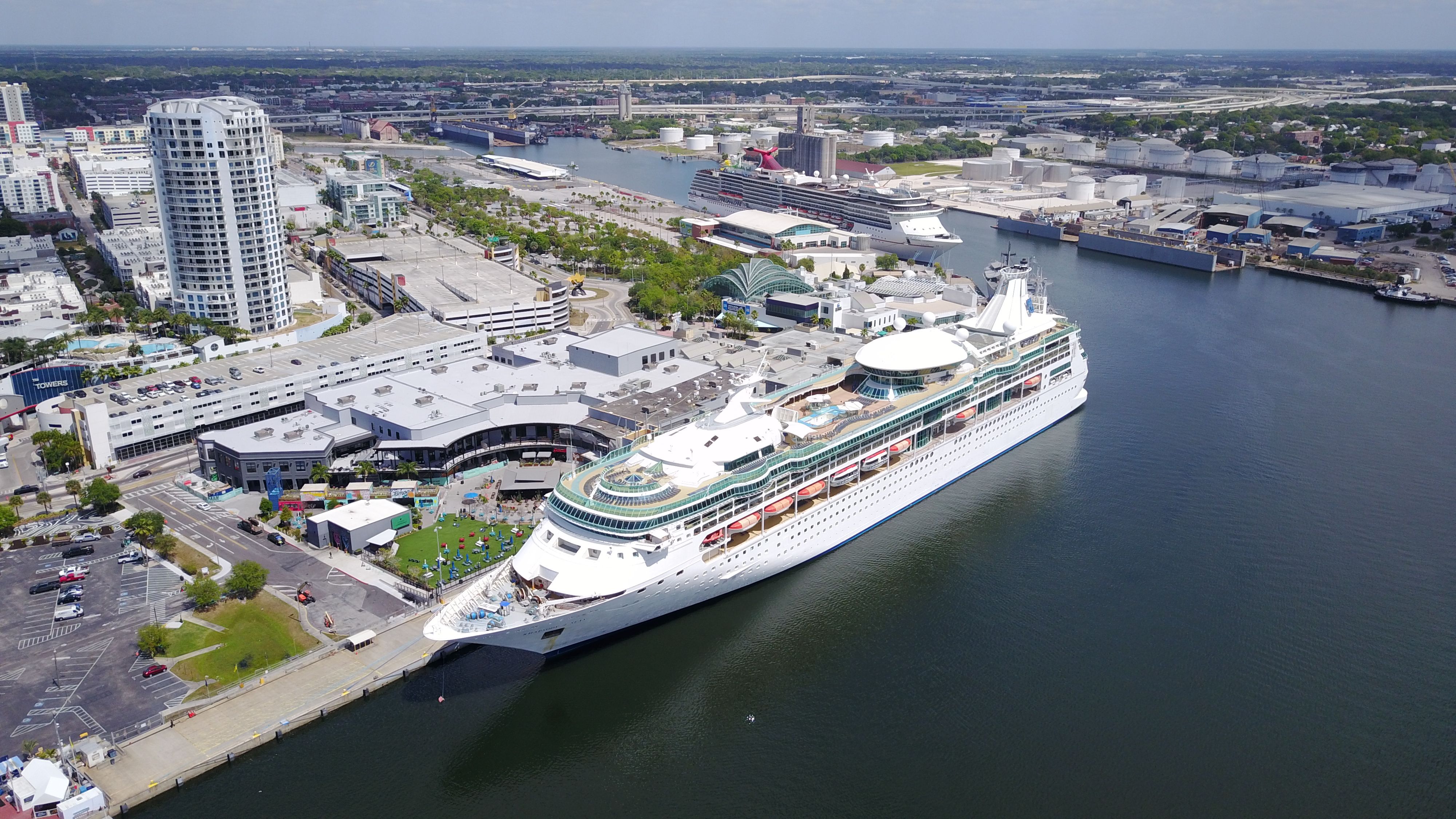 A Royal Caribbean cruise ship docked at Port Tampa Bay, surrounded by city buildings and port facilities under a clear sky.