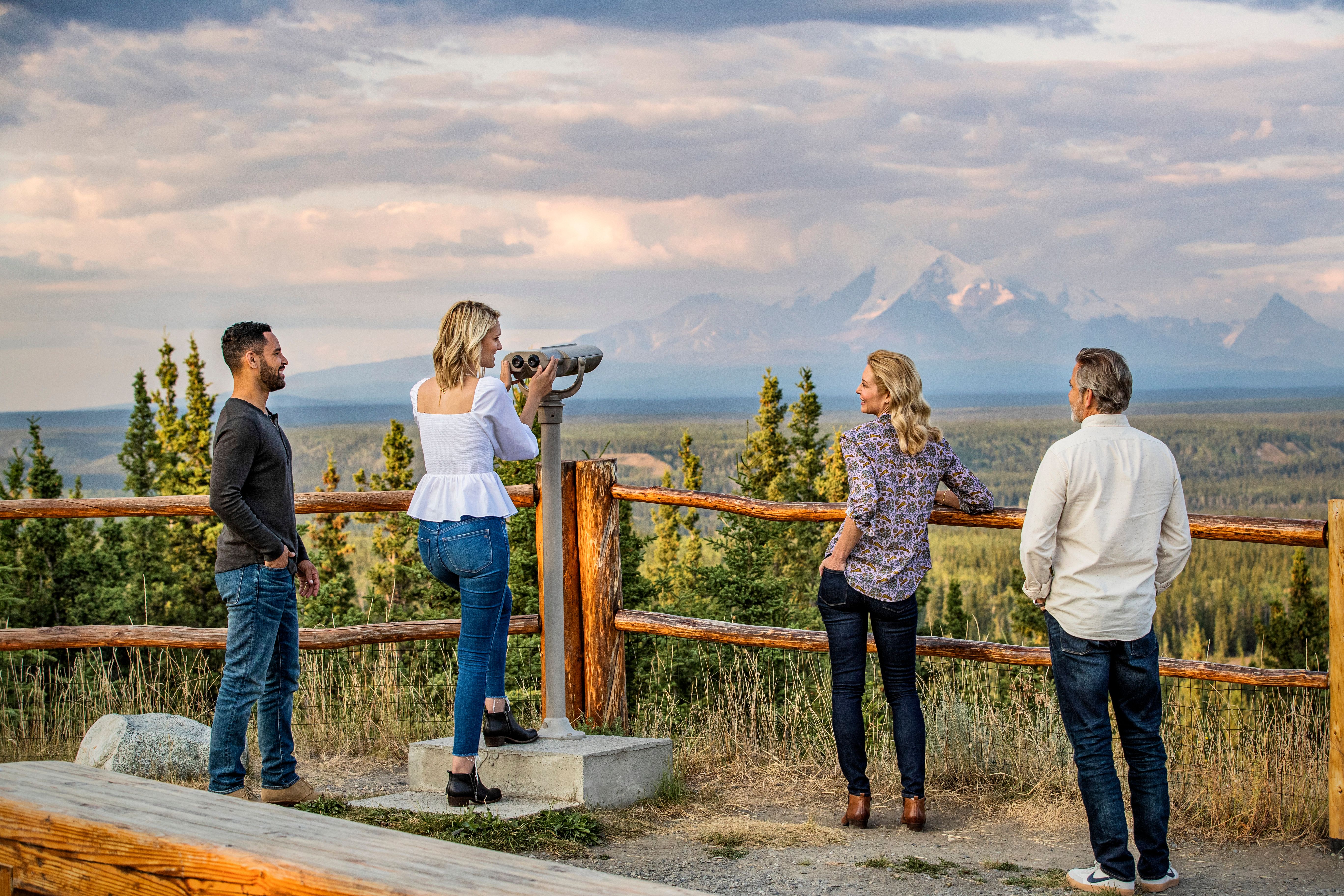 Two couples enjoying a scenic lookout point in Alaska, with mountainous views in the background.