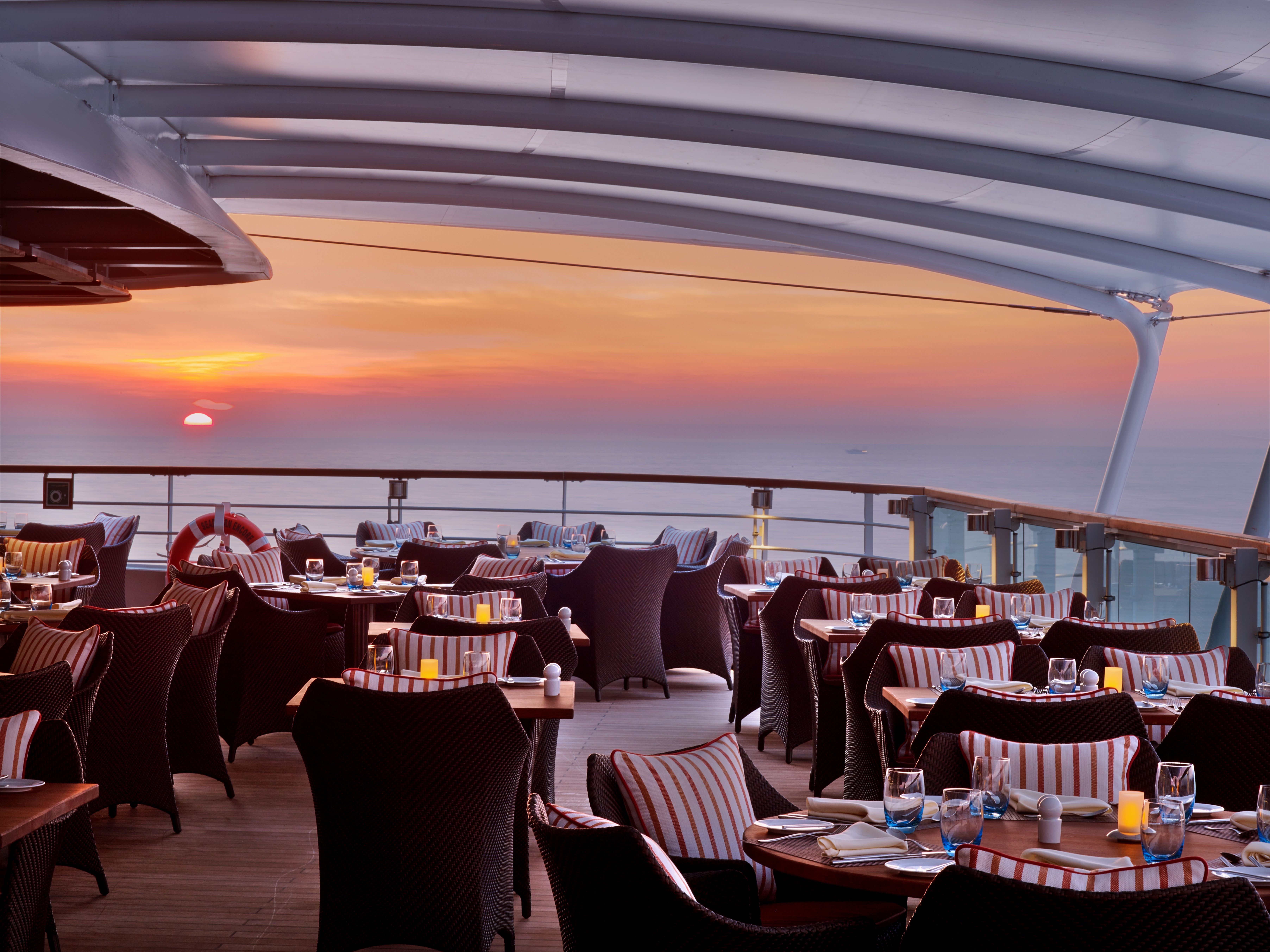 Scenic cruise ship deck dining area at sunset, offering ocean views and comfortable seating.