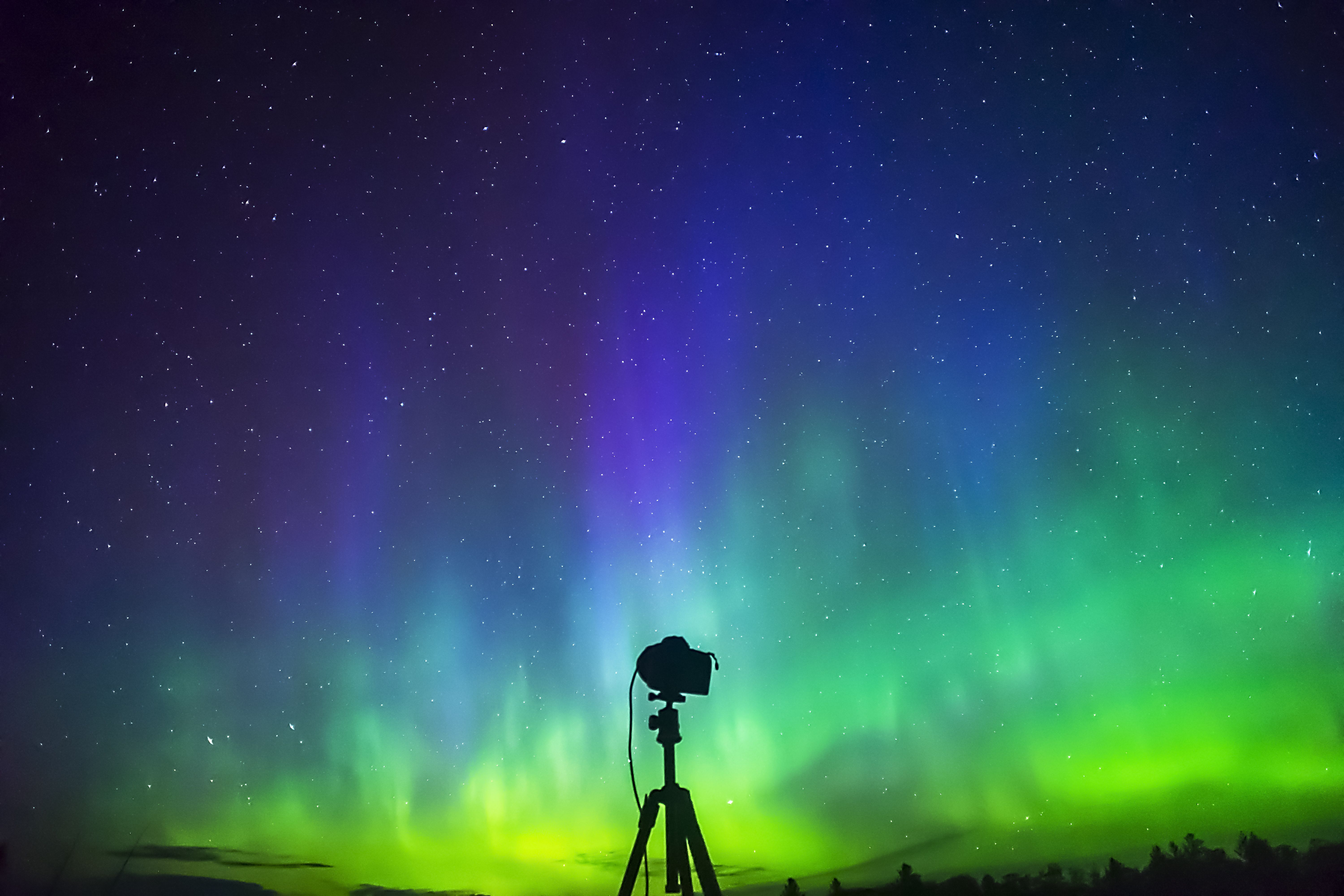 Camera on tripod capturing the northern lights against a starry sky.