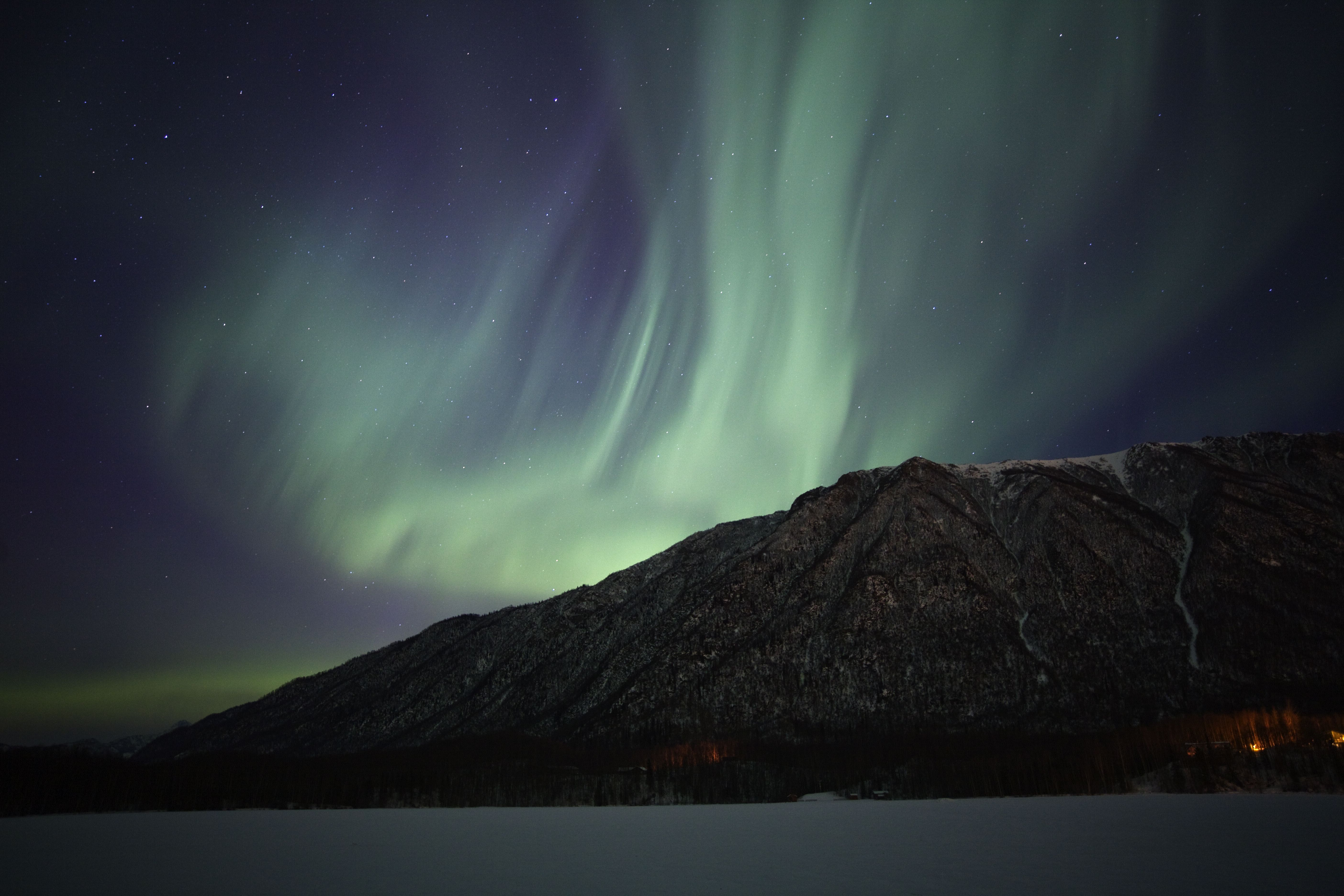 Aurora borealis over a mountainous area in Alaska during winter.