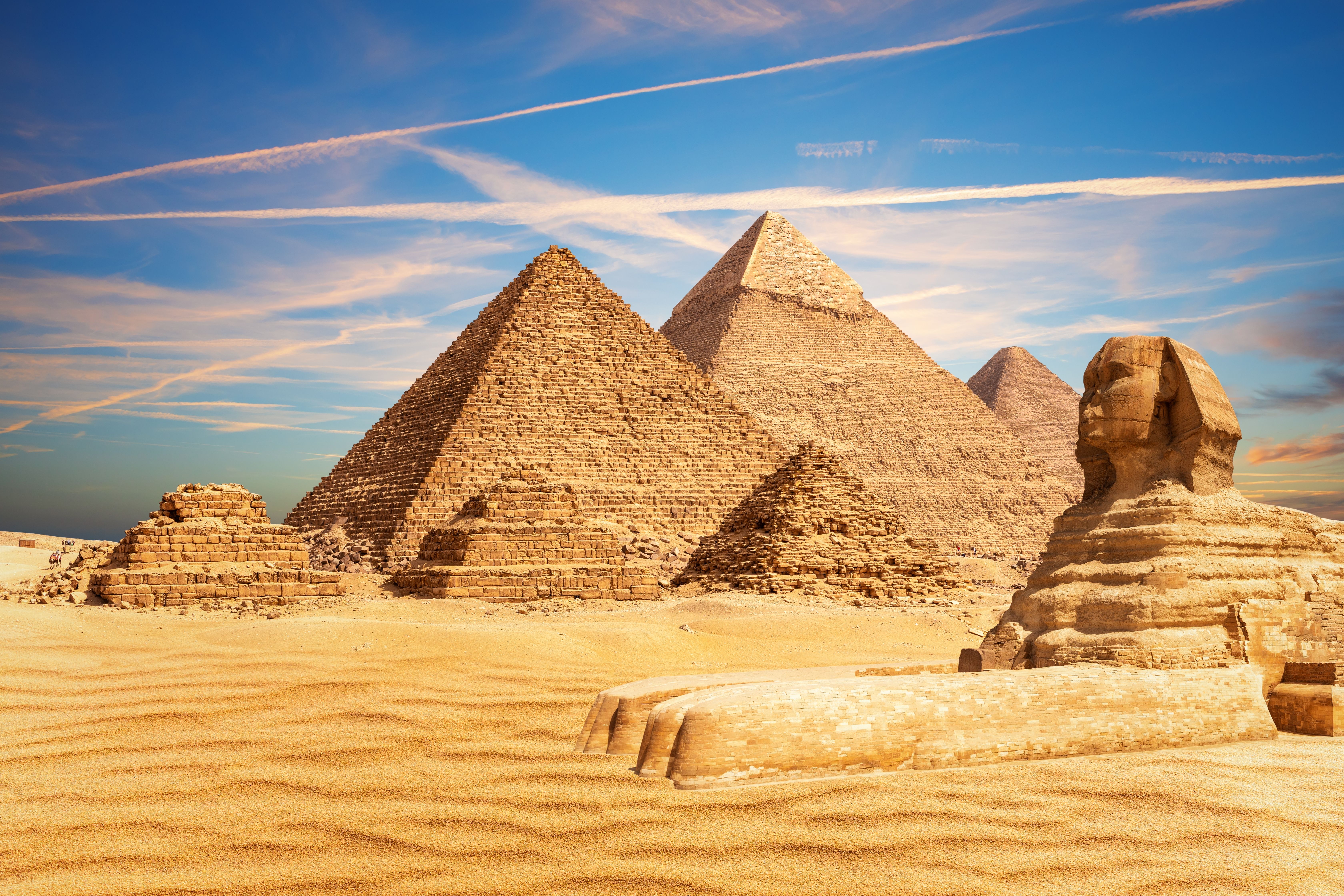 Iconic view of the Pyramids of Giza and the Great Sphinx in Egypt with a clear blue sky and desert sands in the foreground.
