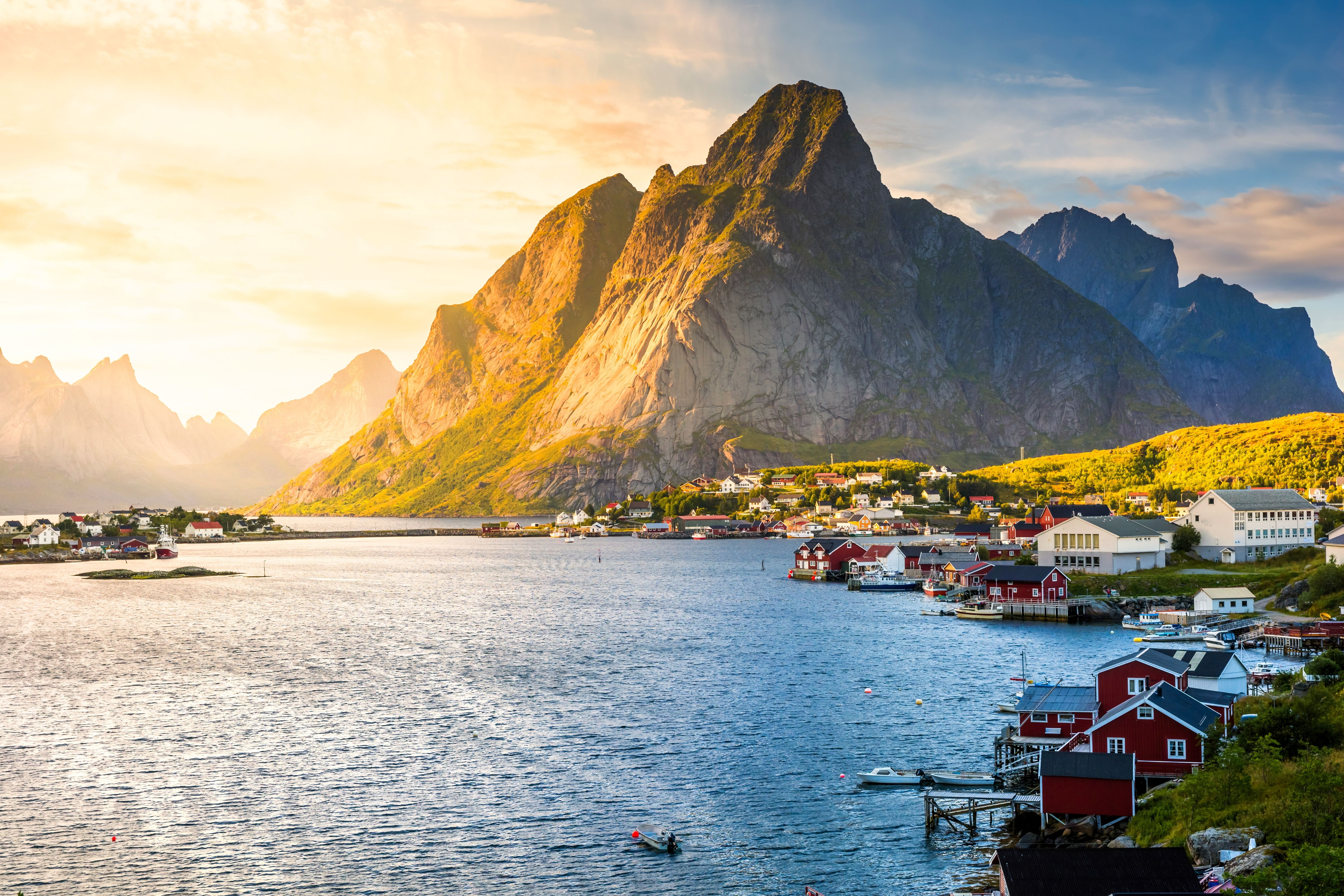 Scenic view of Reine, Norway, featuring colorful houses, rugged mountains, and calm waters under a golden sunset, highlighting the picturesque beauty of the Lofoten Islands.