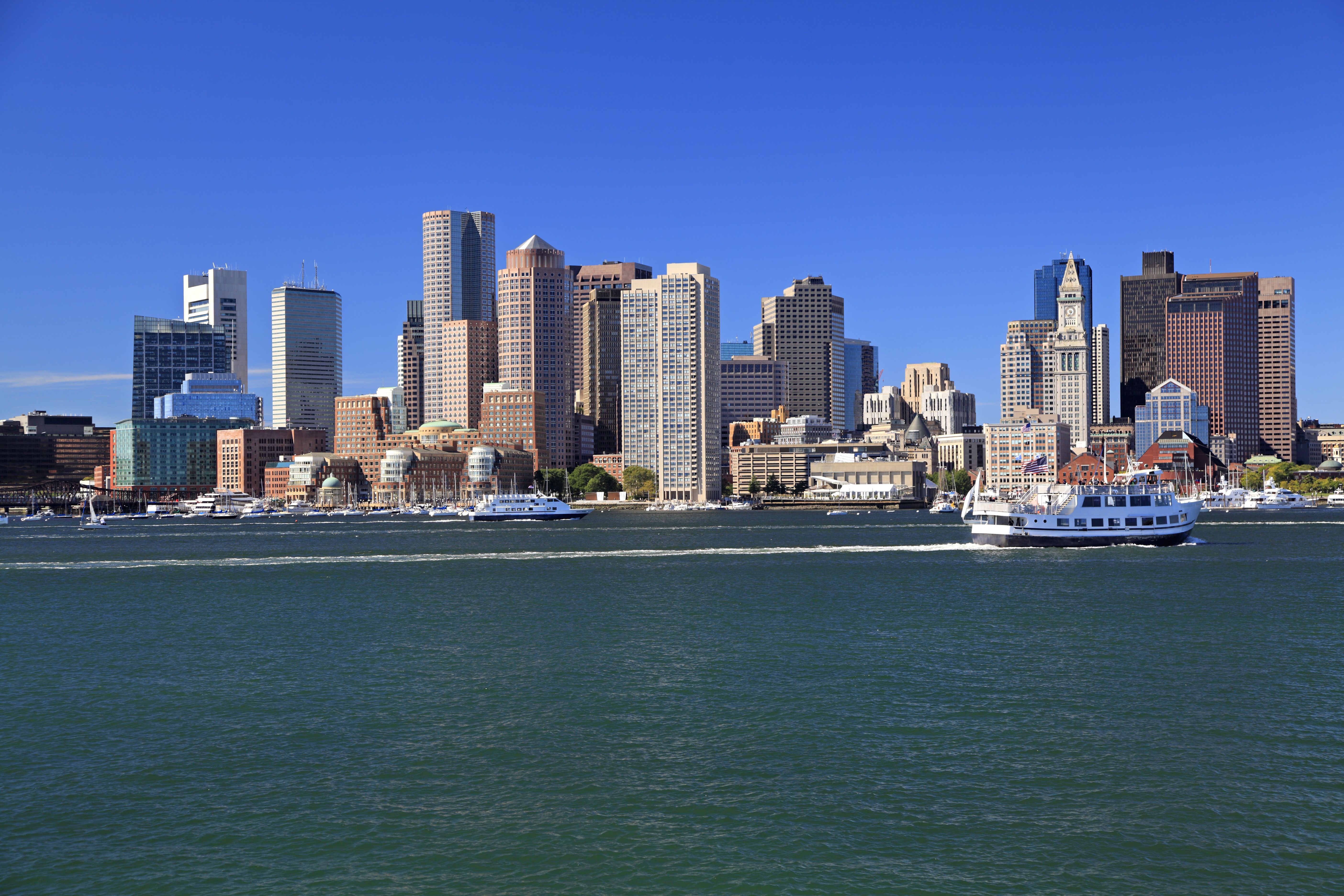 Boston skyline with a cruise ship sailing in the harbor, showcasing the city's iconic skyscrapers and waterfront.