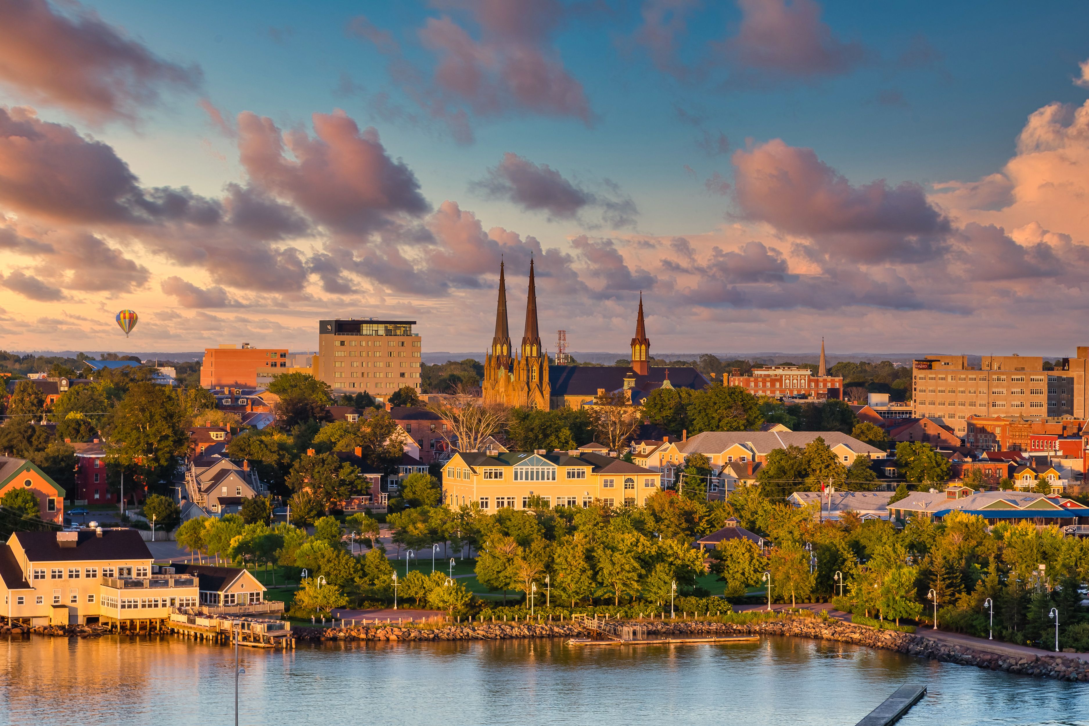 Scenic view of Charlottetown, Canada, featuring historic churches, buildings, and a hot air balloon at sunset.