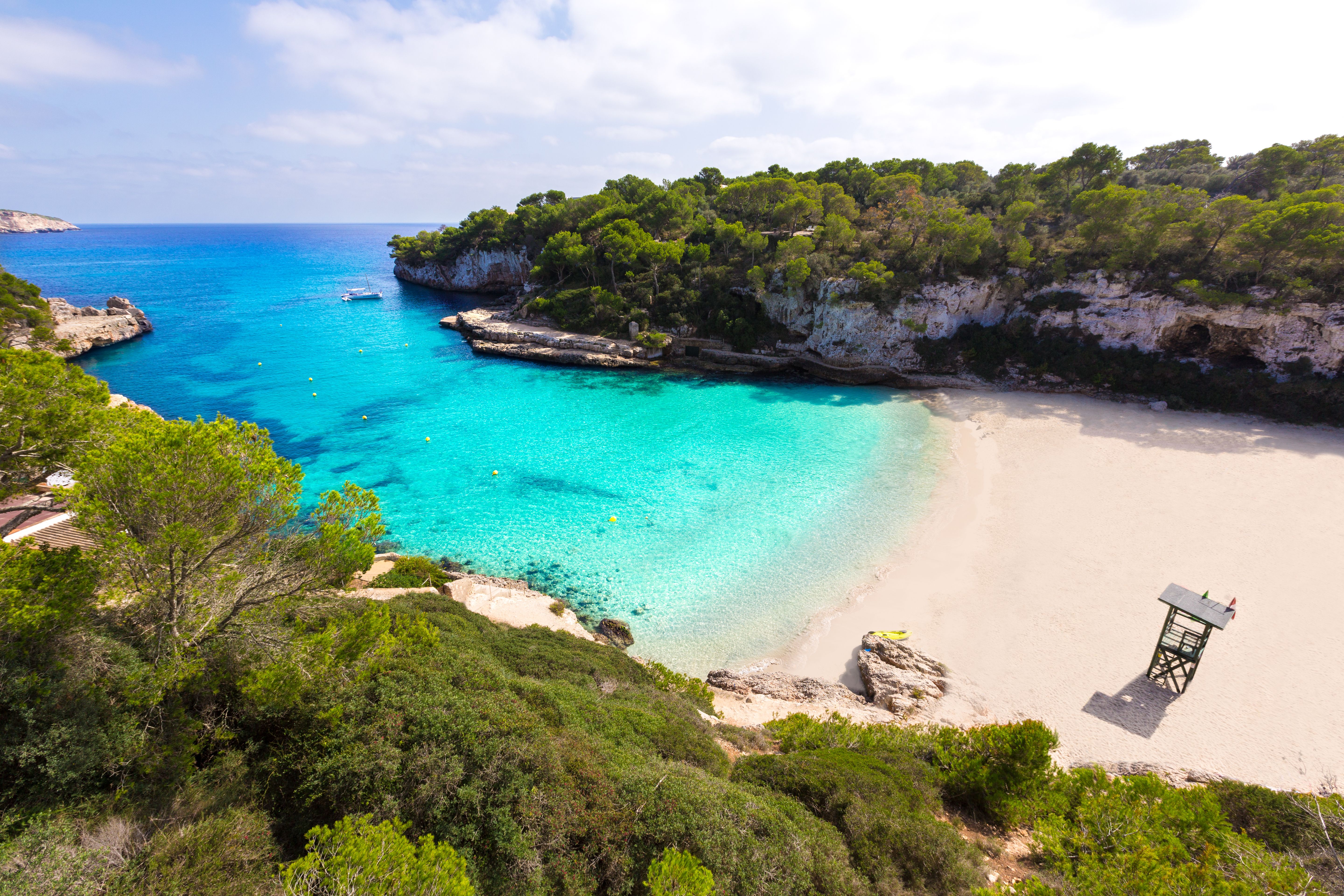 Scenic view of Cala Llombards beach with turquoise waters, white sandy shore, and lush green cliffs in Mallorca, Spain.