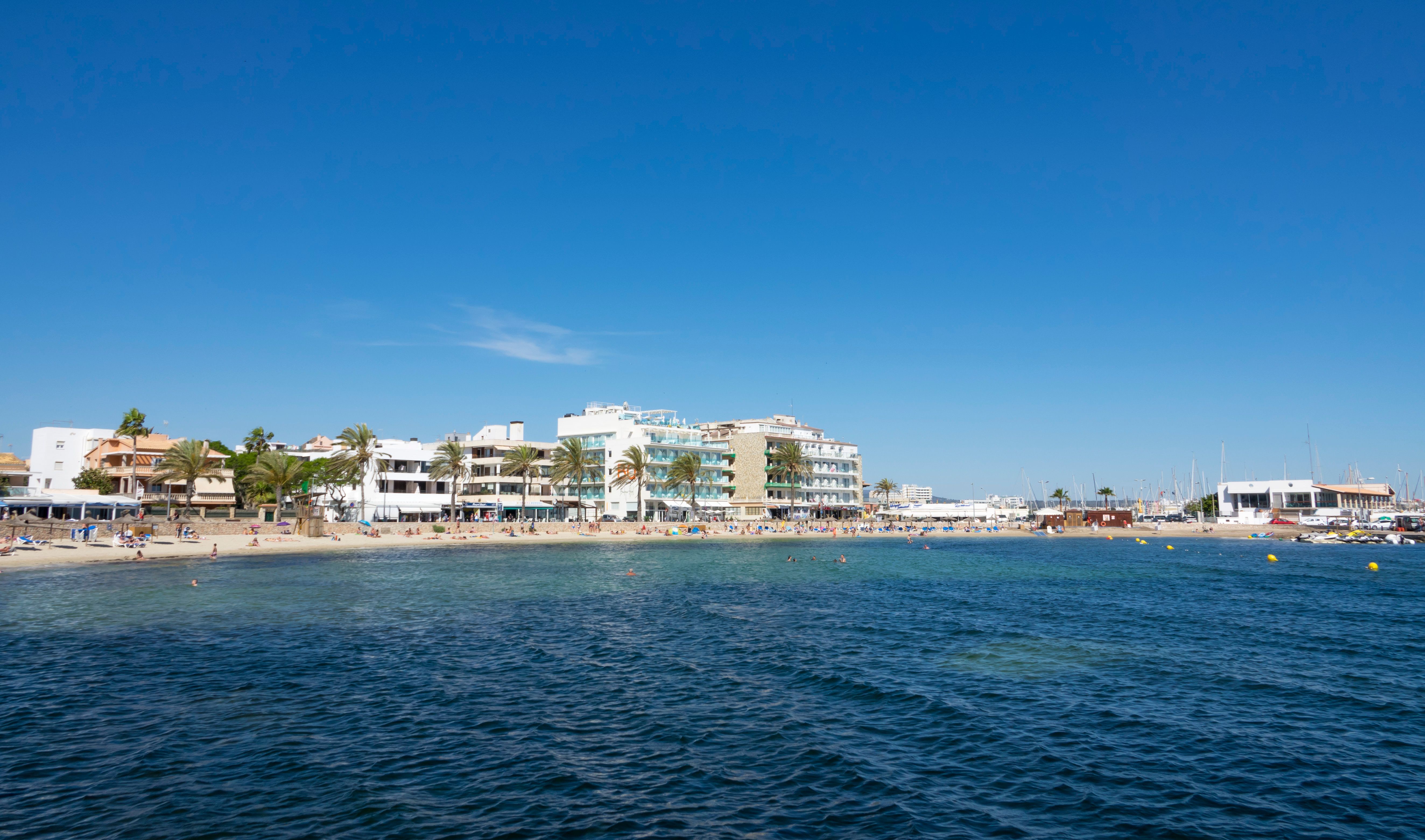 Cala Estancia beach with beachfront buildings, clear blue waters, and sandy shore in Mallorca, Spain