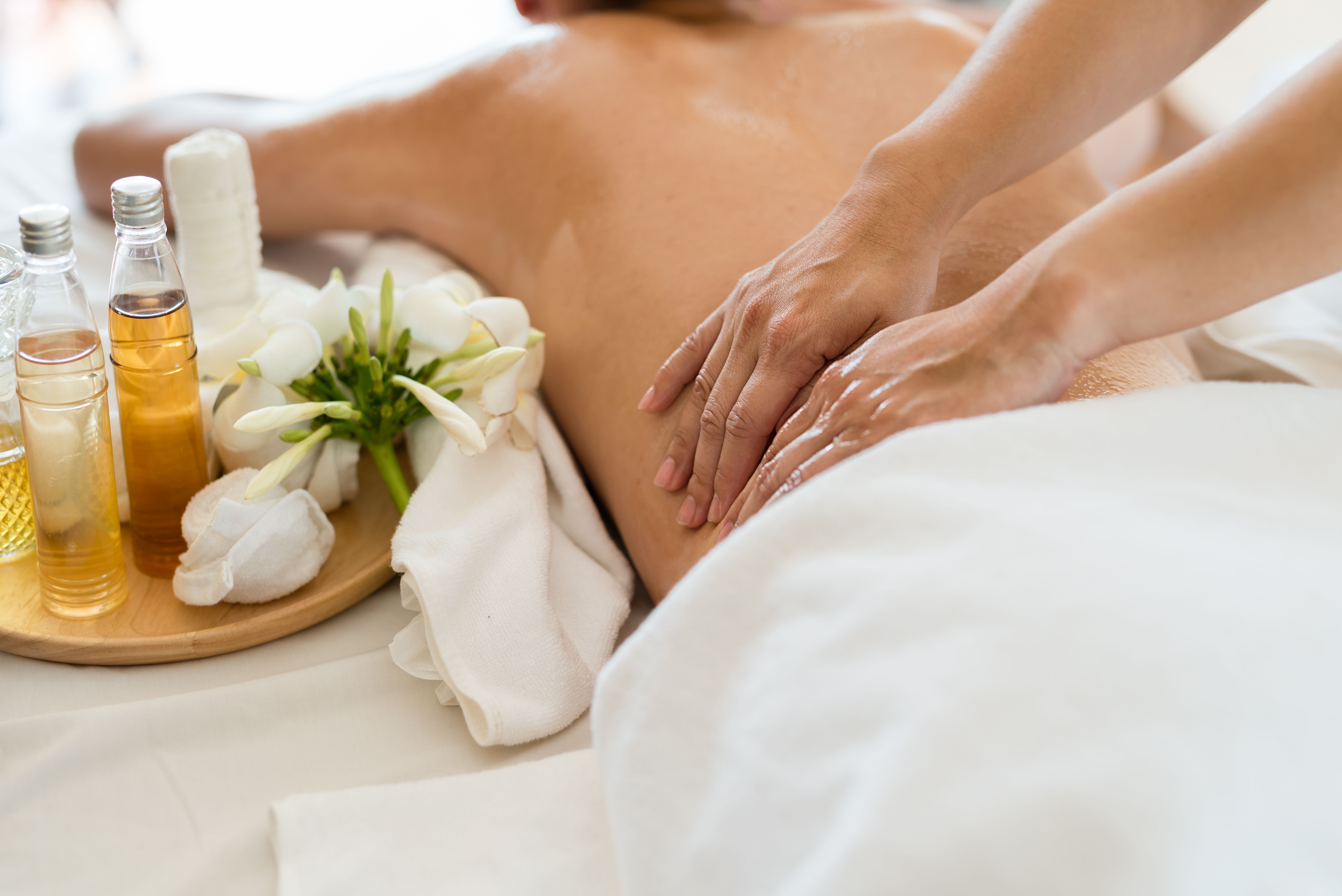 Close-up of a relaxing spa massage treatment with essential oils and white flowers on a wooden tray.