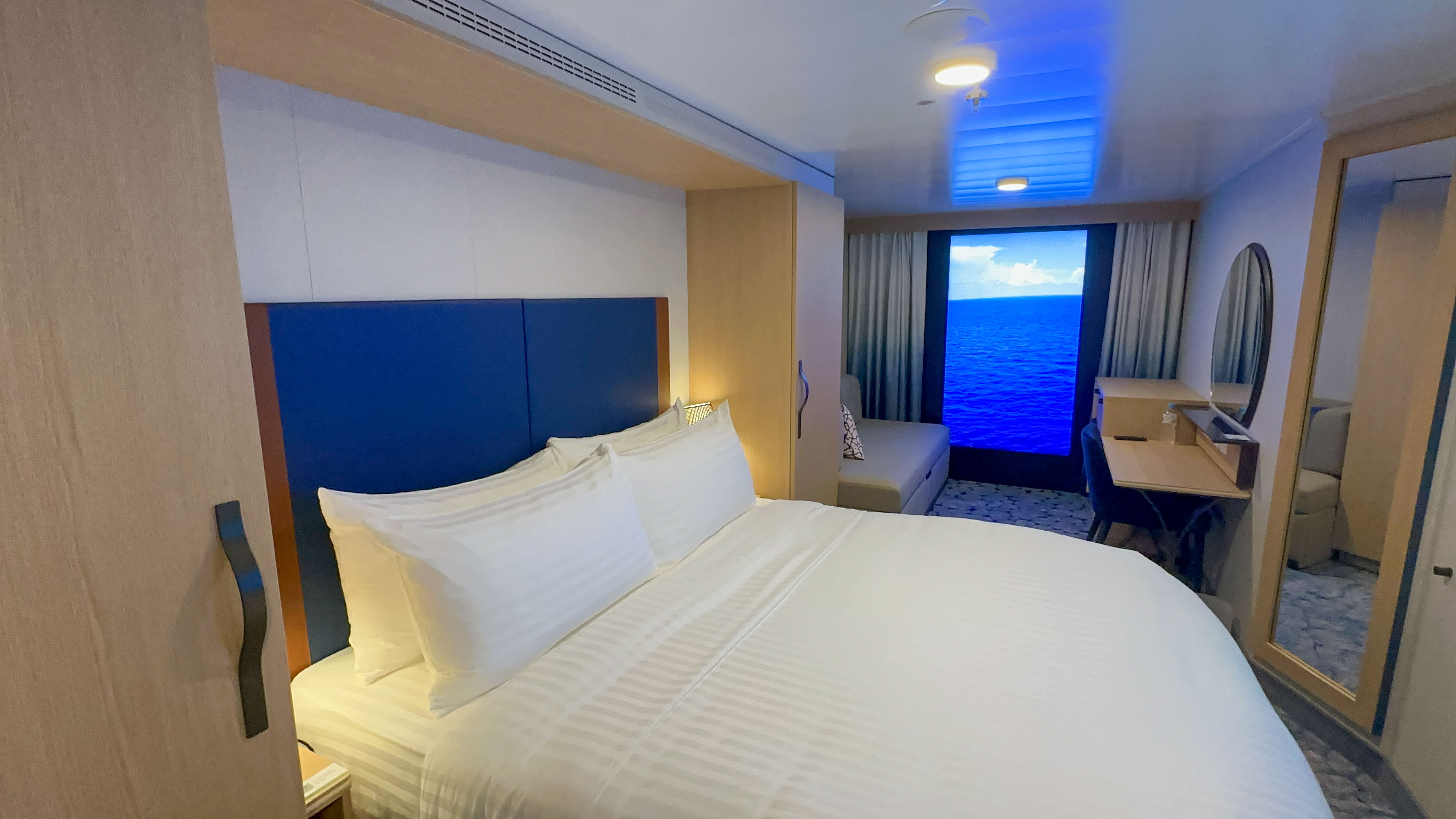 Interior cabin on Royal Caribbean's Utopia of the Seas featuring a virtual balcony, king-size bed, seating area, and a functional desk.