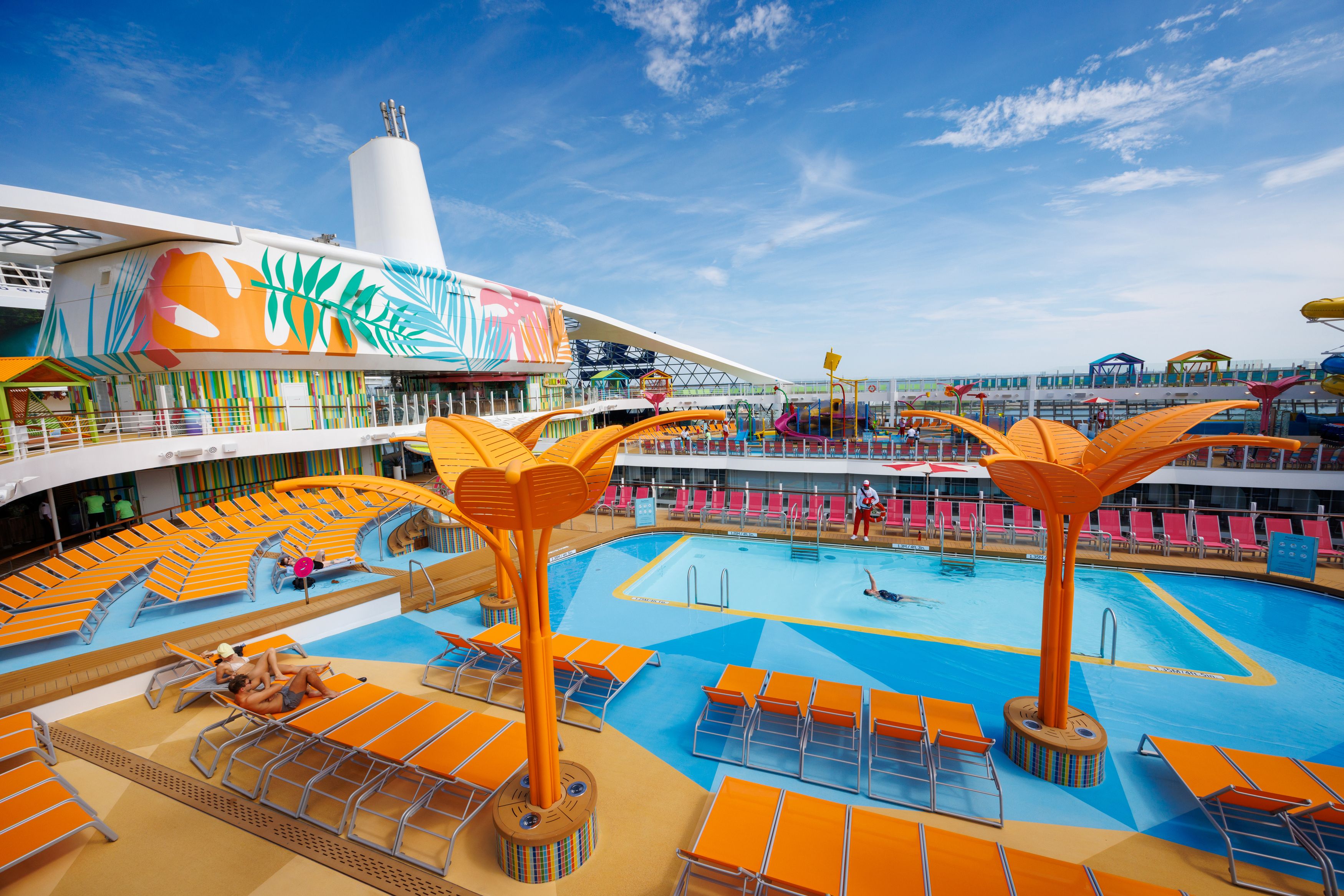 Colorful pool area on Royal Caribbean cruise, featuring bright lounge chairs, umbrellas, and water slides in the background.