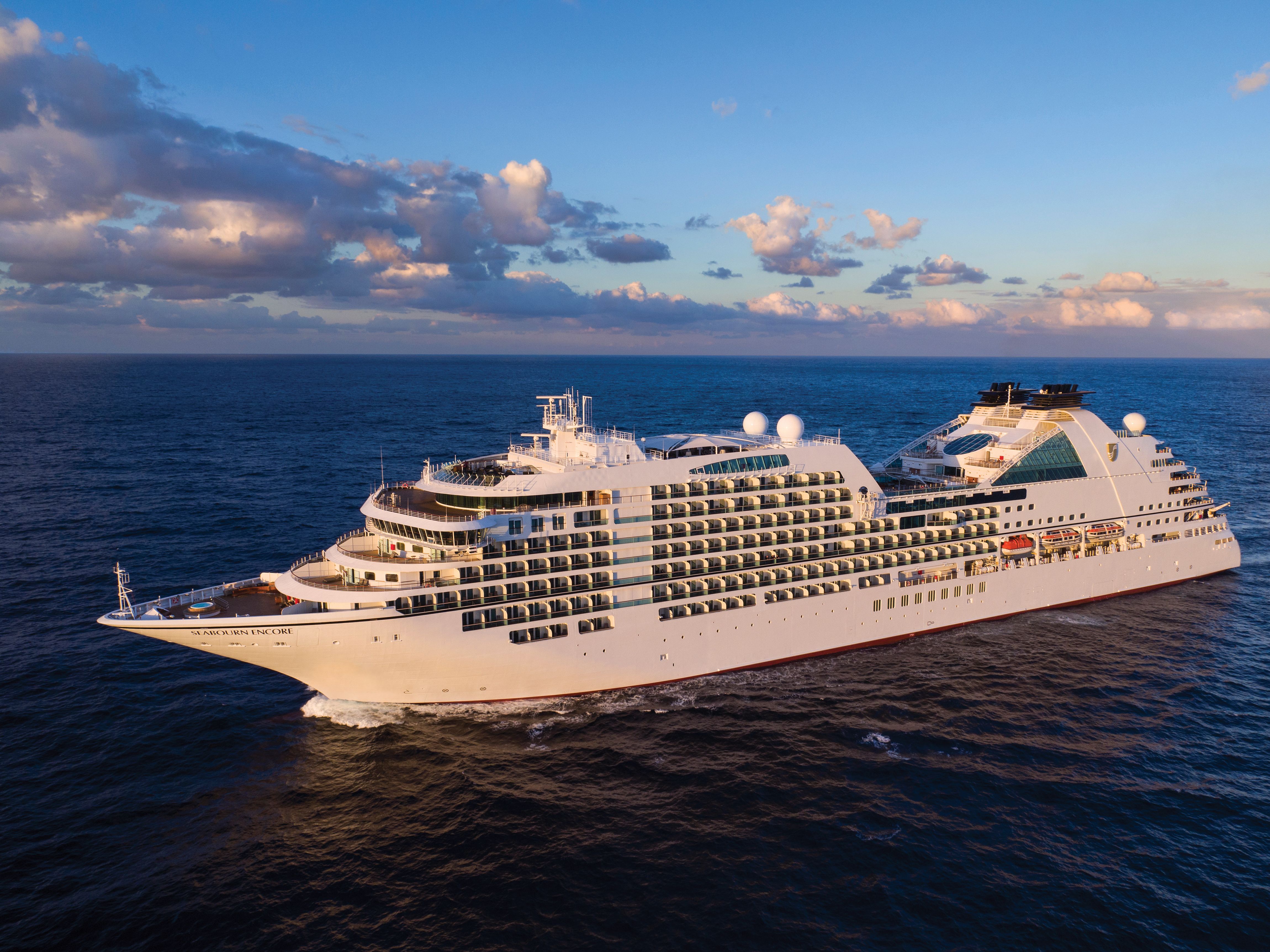 Seabourn Encore cruising at sunset, featuring multiple balcony suites, sleek white exterior, and modern design elements against a vibrant sky.
