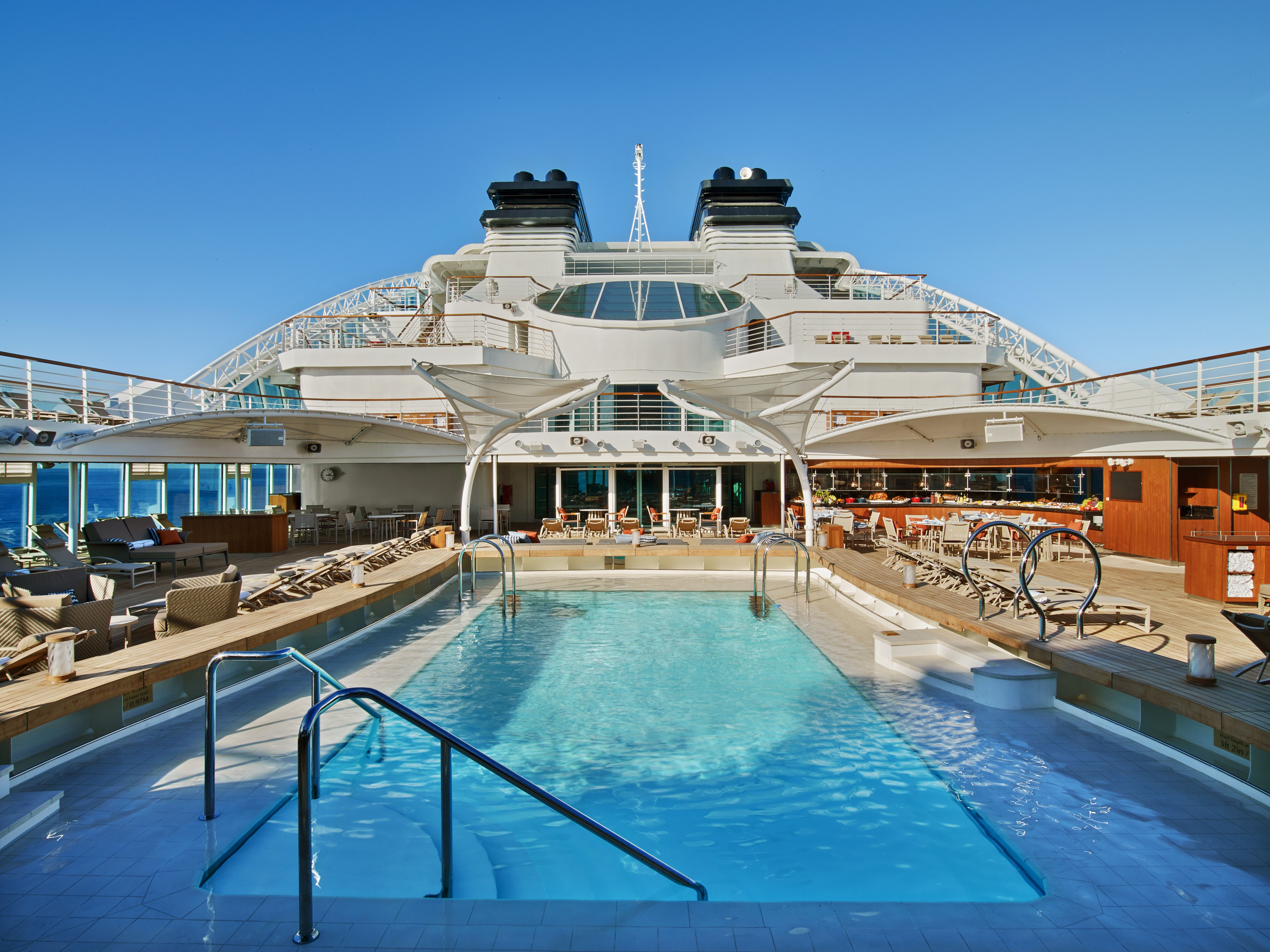 Seabourn Ovation pool deck with a sparkling pool, sun loungers, shaded areas, and multiple deck levels against a clear blue sky.