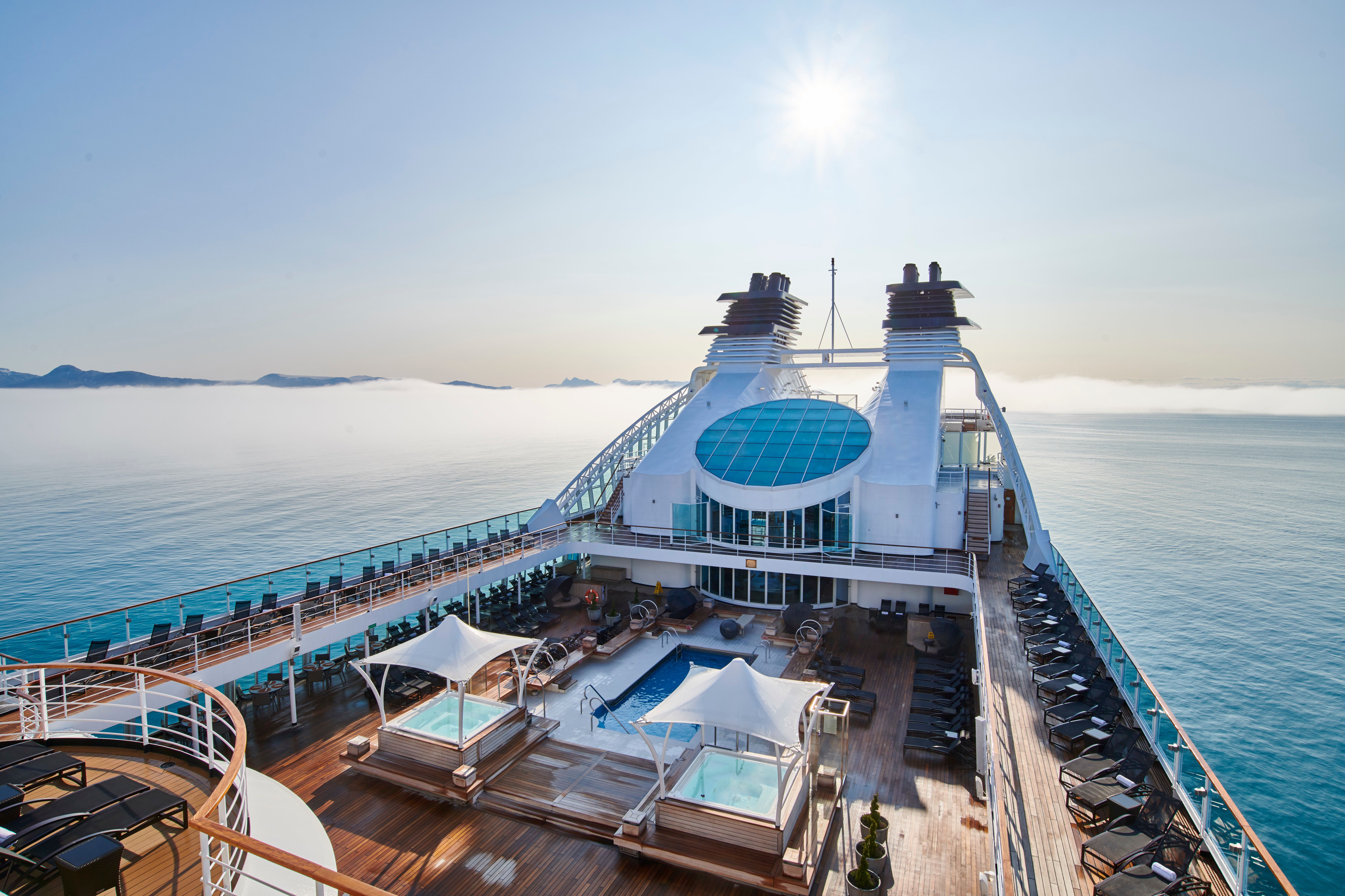 Aerial view of Seabourn Sojourn's pool deck with hot tubs, sun loungers, and panoramic ocean views under a clear sky.