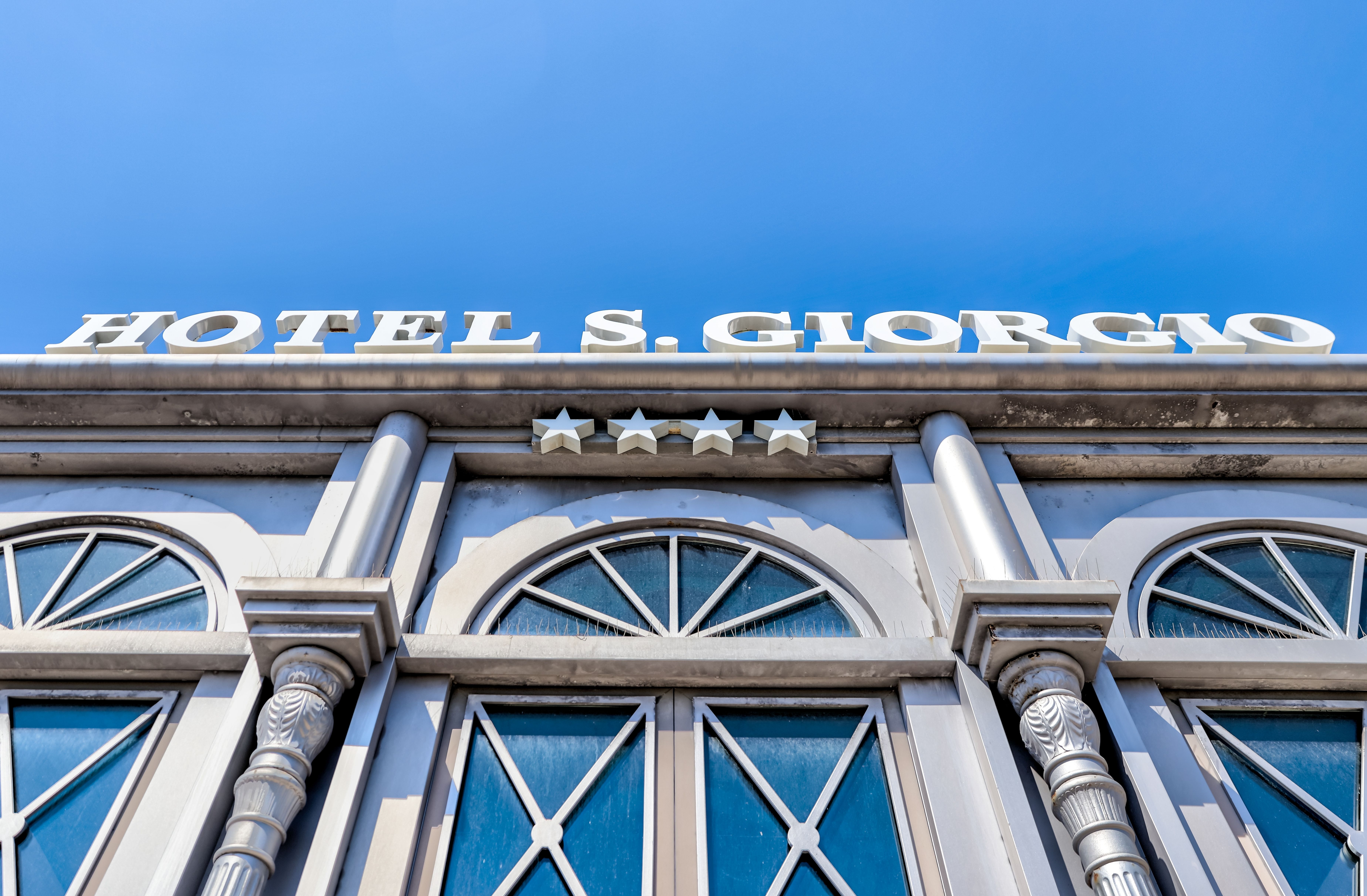 Close-up of Hotel San Giorgio's four-star sign against a clear blue sky.