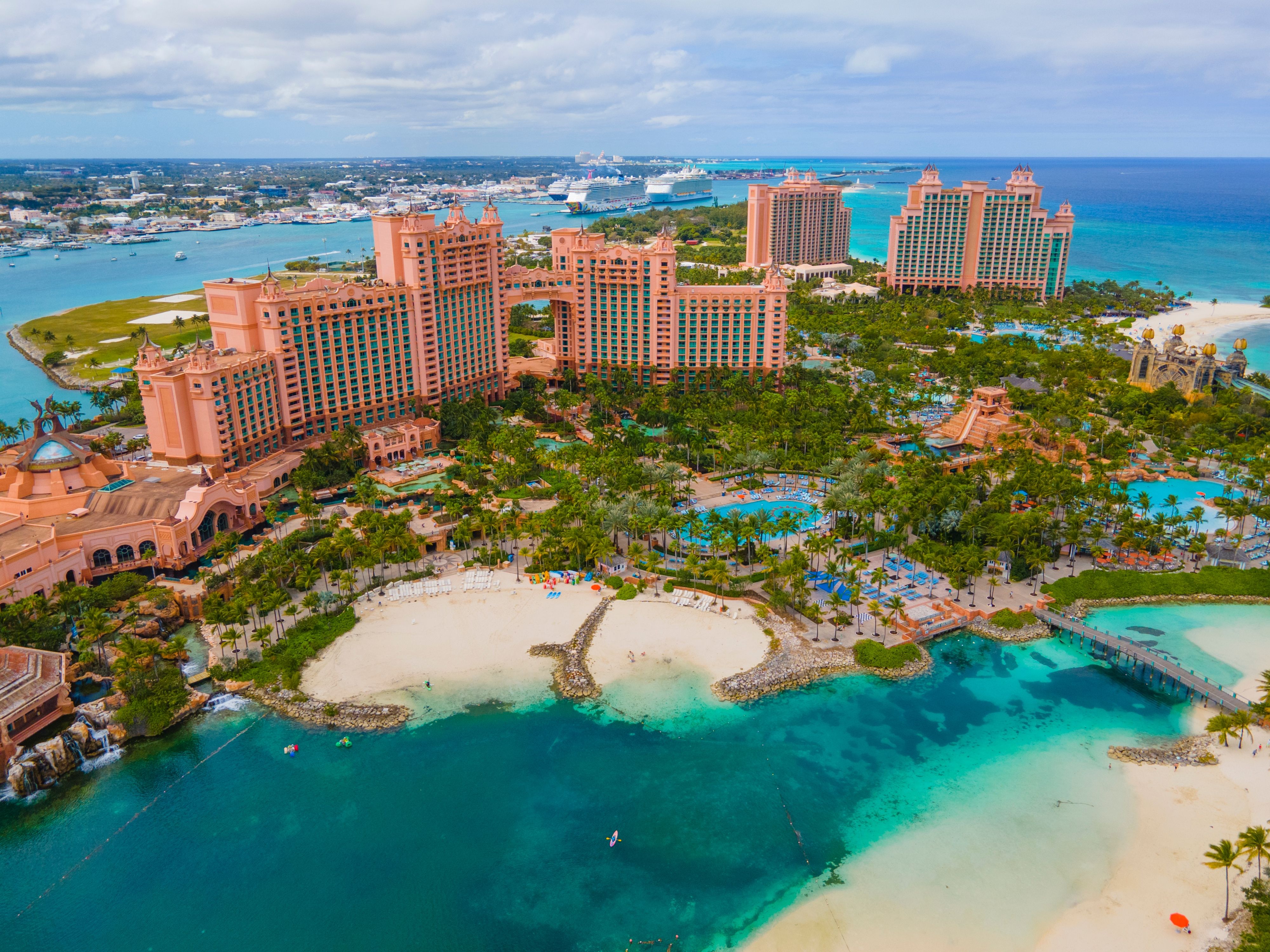 Aerial view of Atlantis Paradise Island resort in Nassau, Bahamas, featuring expansive pools, lush greenery, and a private beach with turquoise waters, with cruise ships docked nearby.