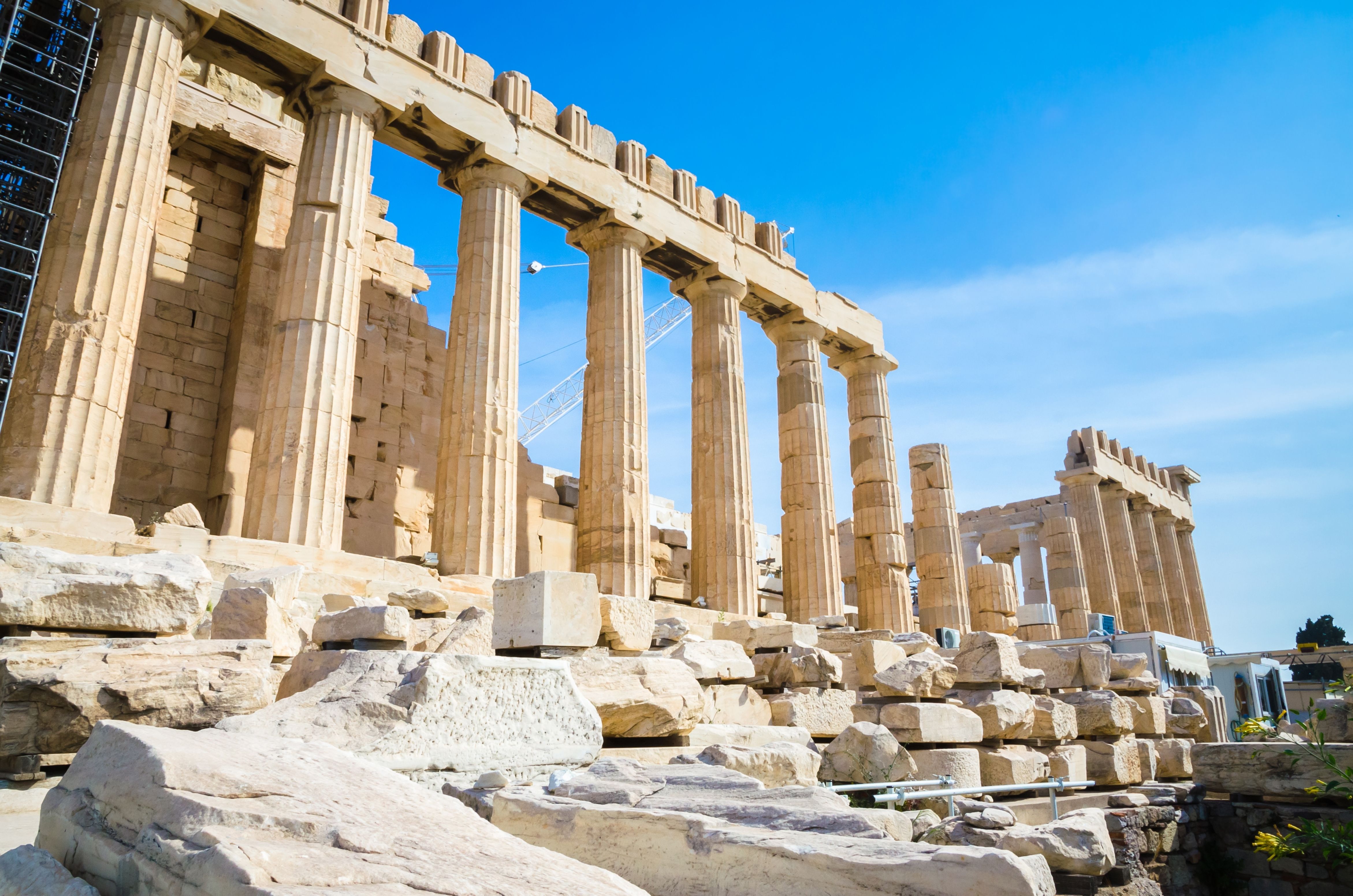 The ancient Parthenon of the Acropolis in Athens, Greece, with its towering marble columns and partially restored structure, basking in sunlight against a clear blue sky.