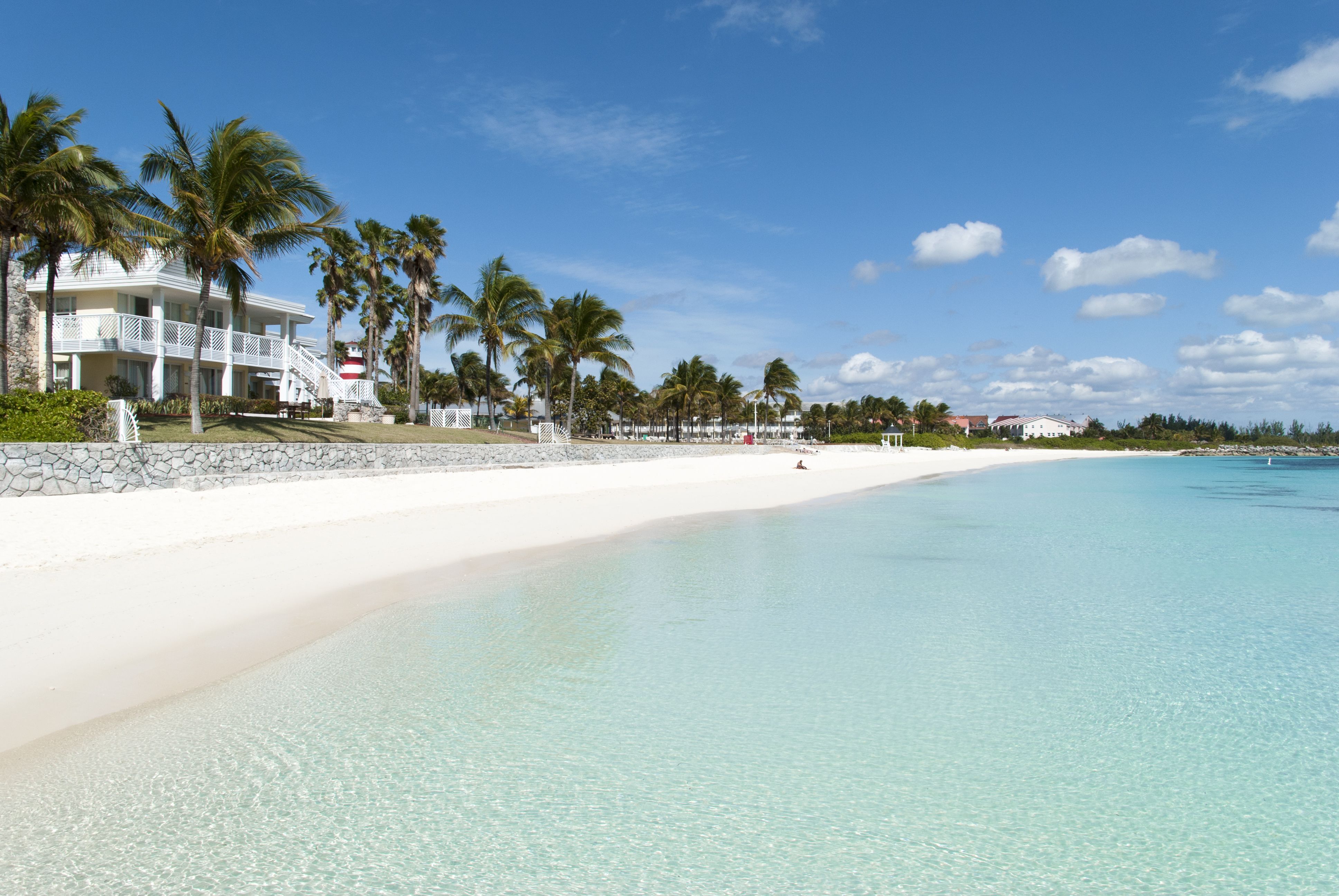 Pristine white sand beach and turquoise waters in Freeport, Bahamas, with palm trees and beachfront homes, offering a tranquil escape on Oceania Cruises' Beach Hideaway excursion