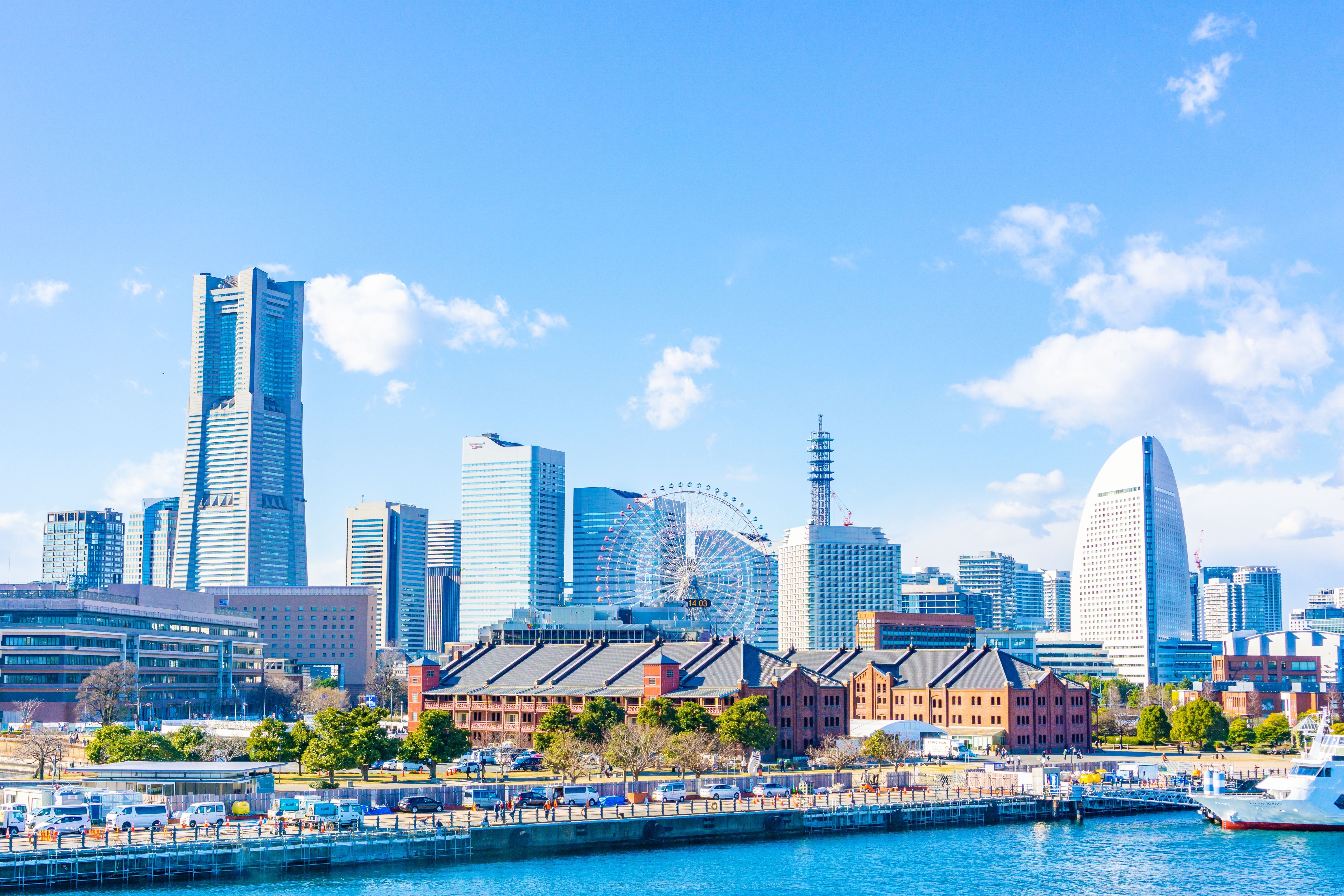 Yokohama skyline with iconic landmarks like the Landmark Tower, a Ferris wheel, and waterfront warehouses under a clear blue sky, part of Oceania Cruises' Yokohama Highlights excursion.