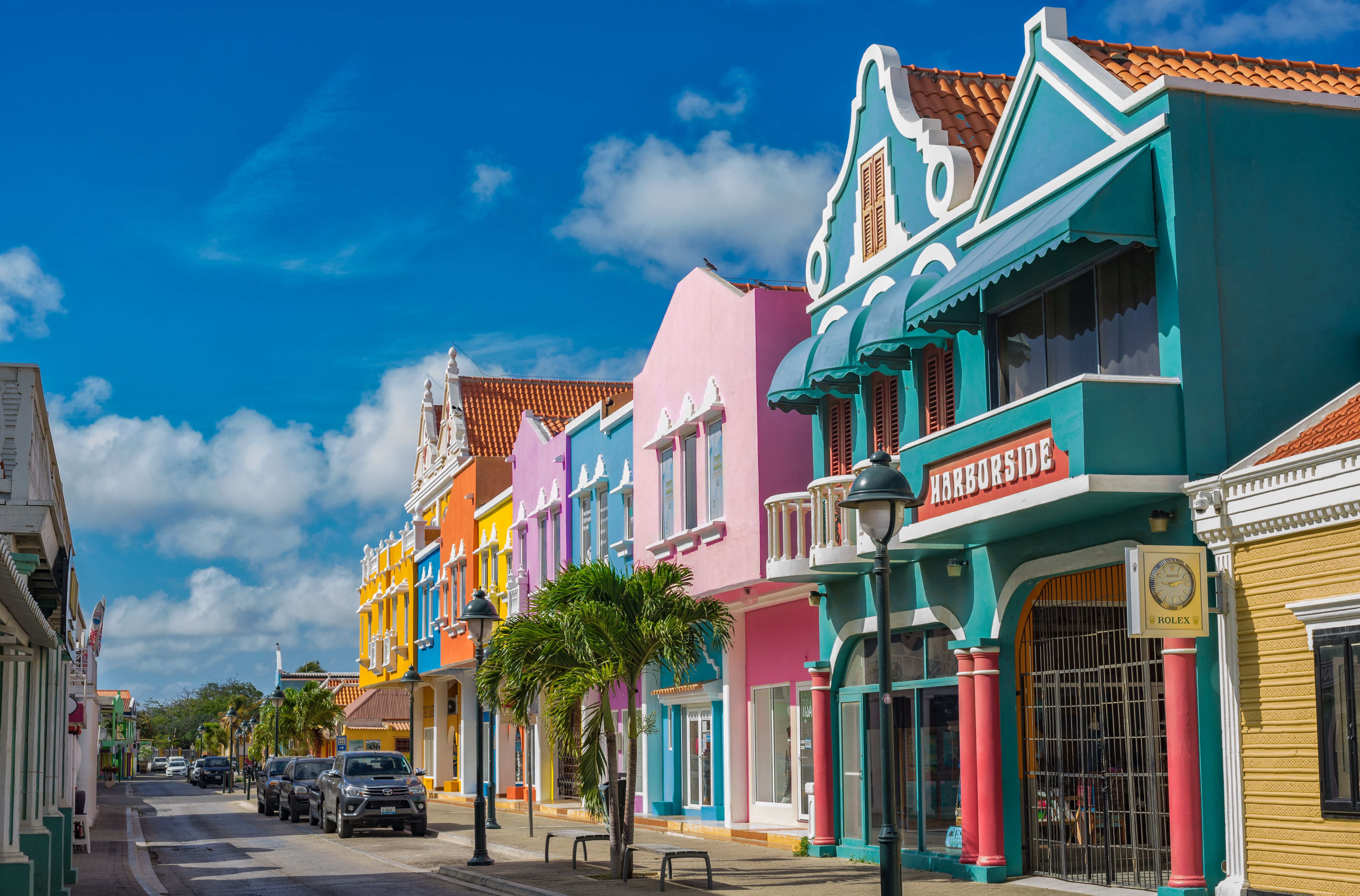 Colorful colonial-style buildings along a vibrant street in Oranjestad, Aruba, showcasing Dutch-Caribbean architecture under a bright blue sky.