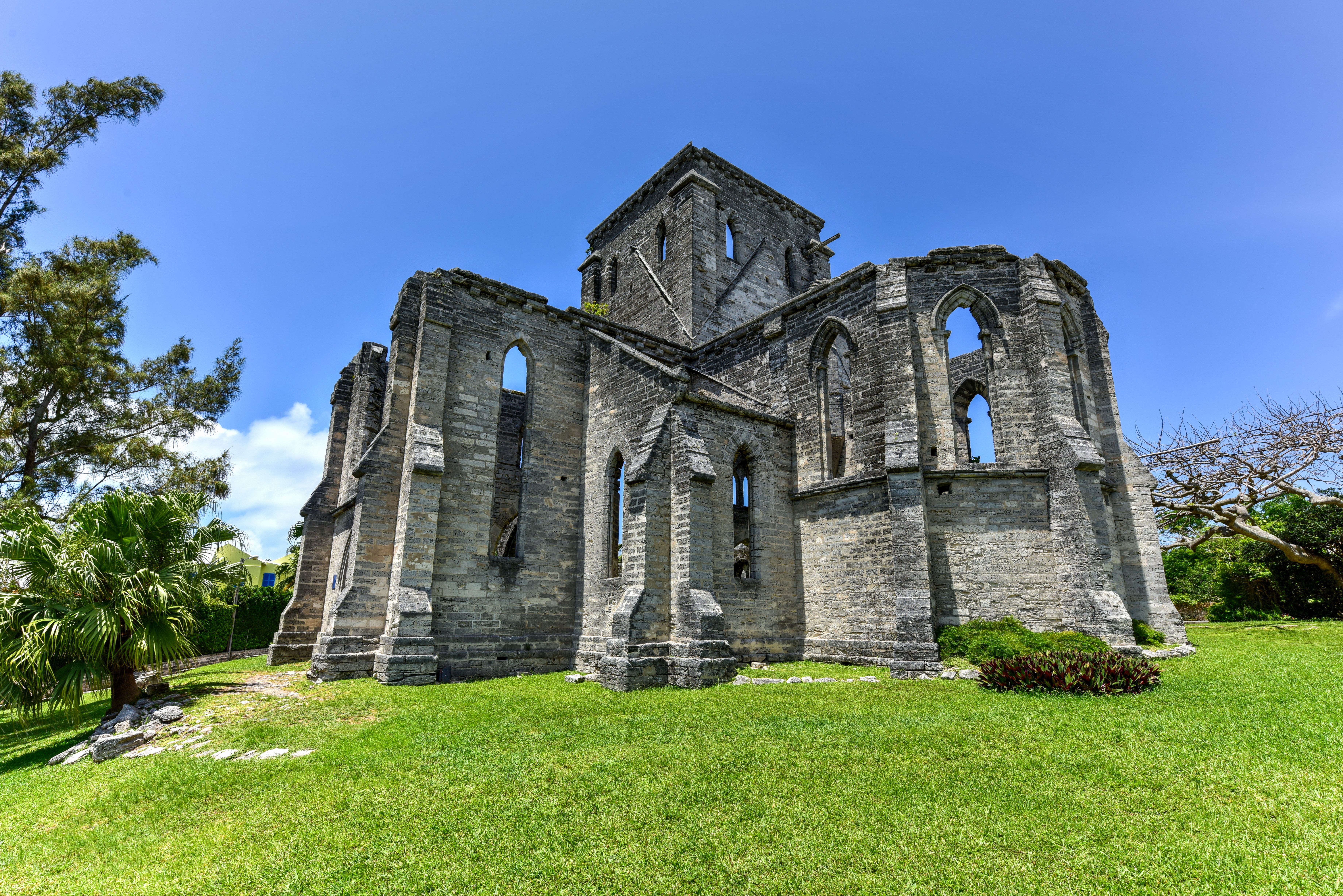 Unfinished Church ruins in St. George's, Bermuda, featuring Gothic-style architecture, set on a lush green lawn under a bright blue sky.