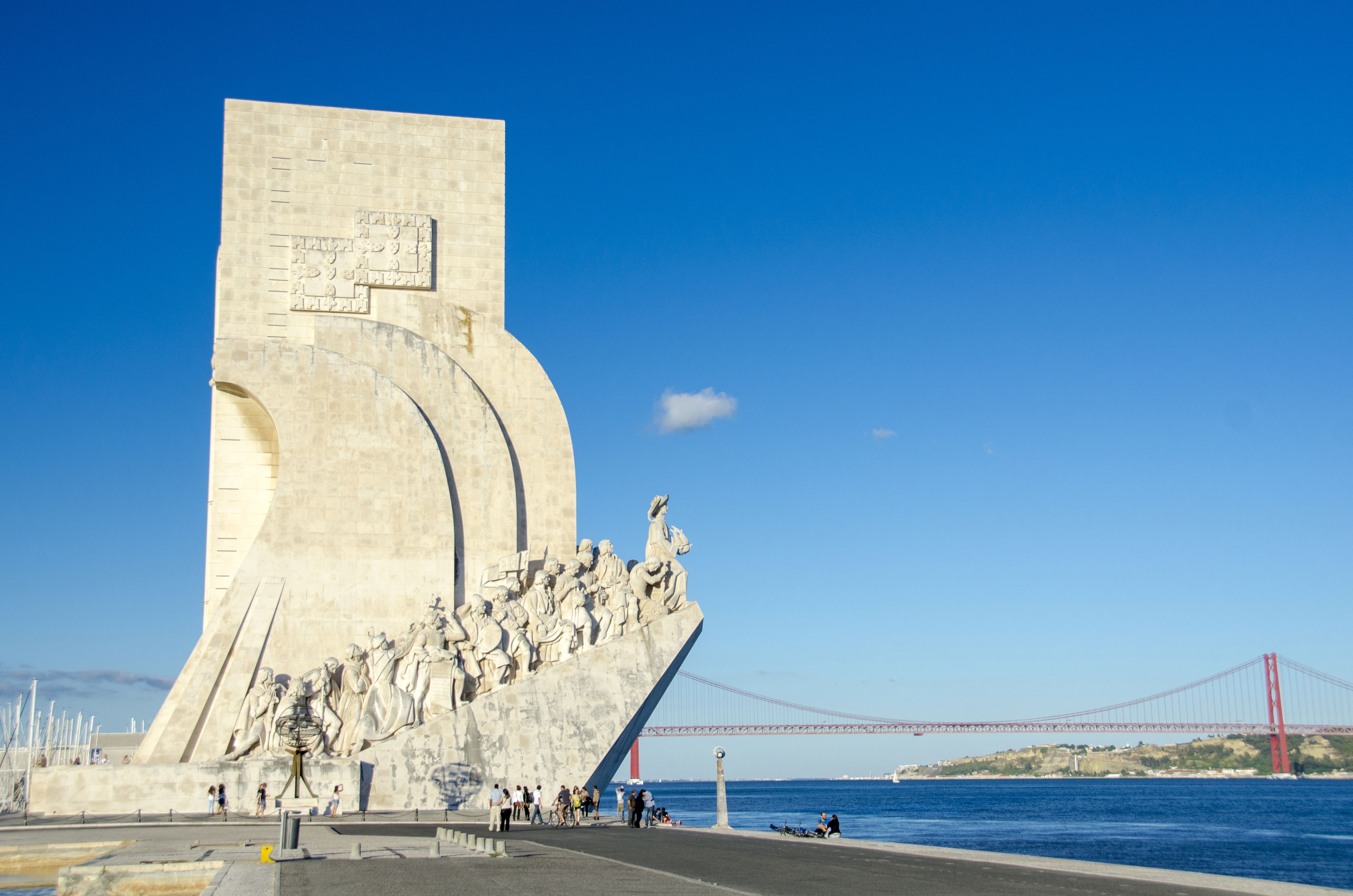 Padrão dos Descobrimentos monument in Lisbon, Portugal, honoring explorers, with the Tagus River and 25 de Abril Bridge in the background under a clear blue sky.