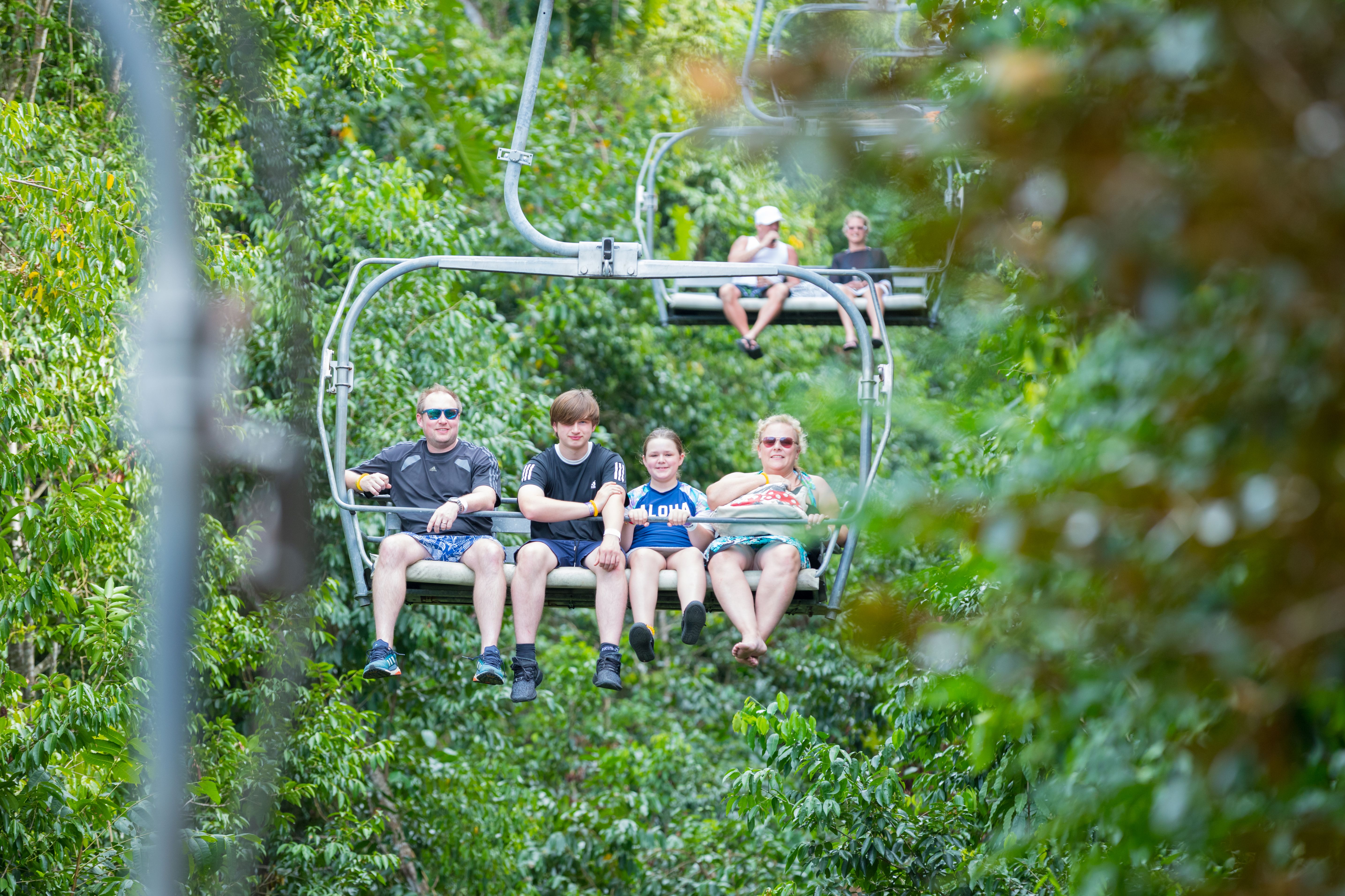 Family enjoying a scenic chairlift ride through lush green foliage in Ocho Rios, Jamaica, offering panoramic views of the rainforest.