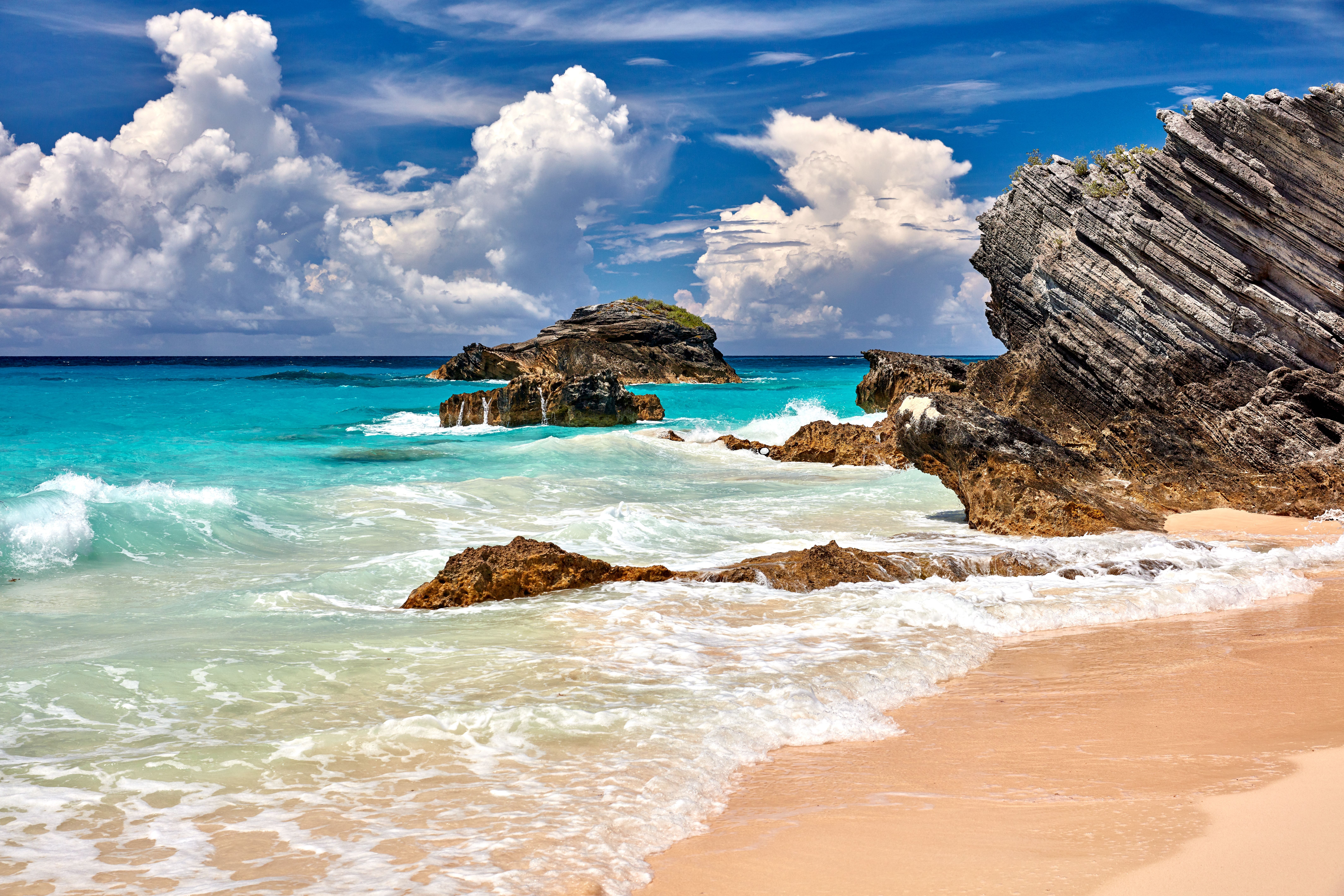 A stunning Bermuda beach with pink sand, turquoise waters, and dramatic rock formations under a bright blue sky—showcasing the island’s year-round mild weather.
