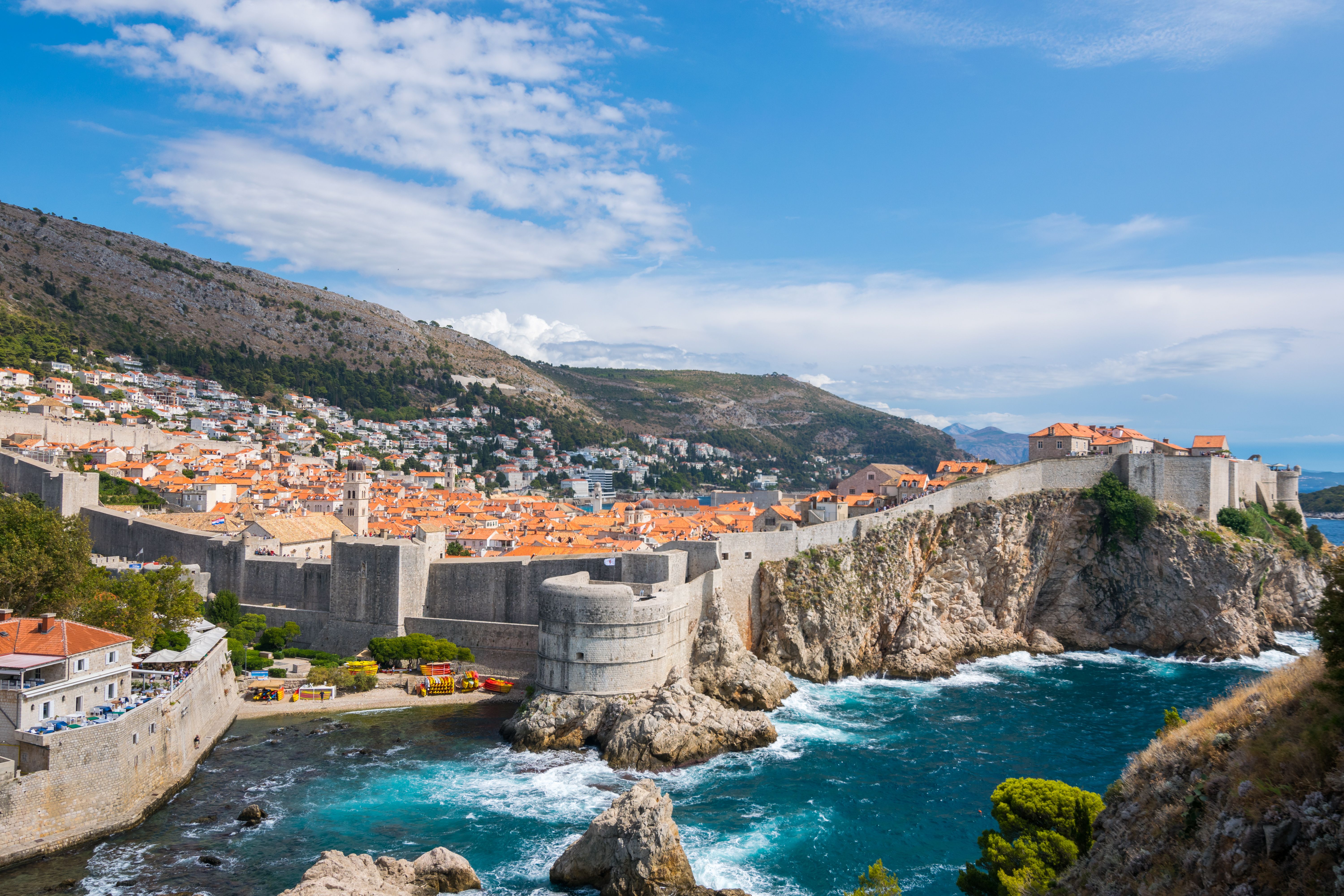 Scenic view of Dubrovnik, Croatia, featuring the historic Old Town, medieval stone walls, and the Adriatic Sea under a bright blue sky.