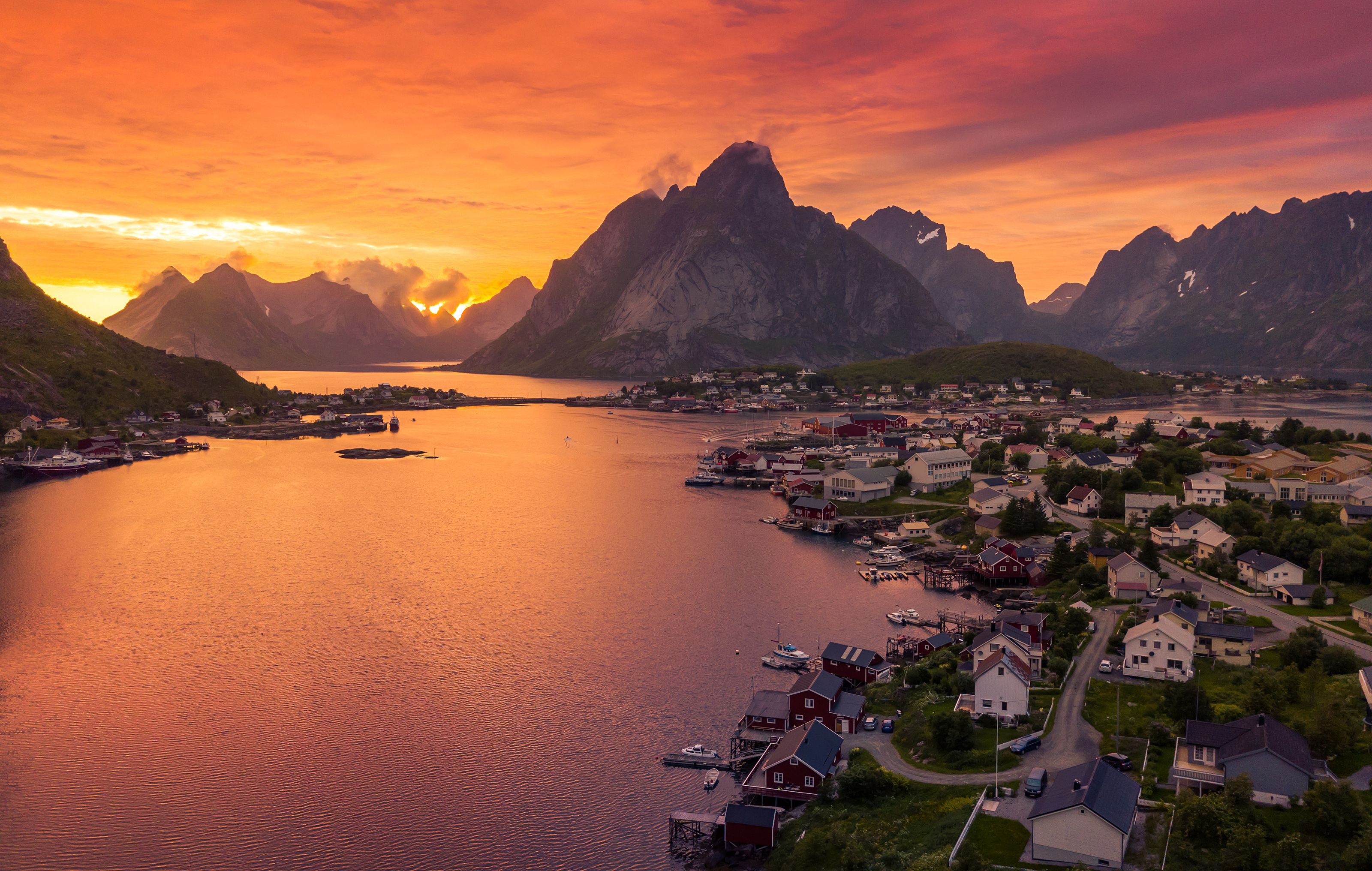 Scenic view of Reine, a fishing village in Norway’s Lofoten Islands, at sunset, with dramatic mountains, calm waters, and colorful houses reflecting in the fjord.