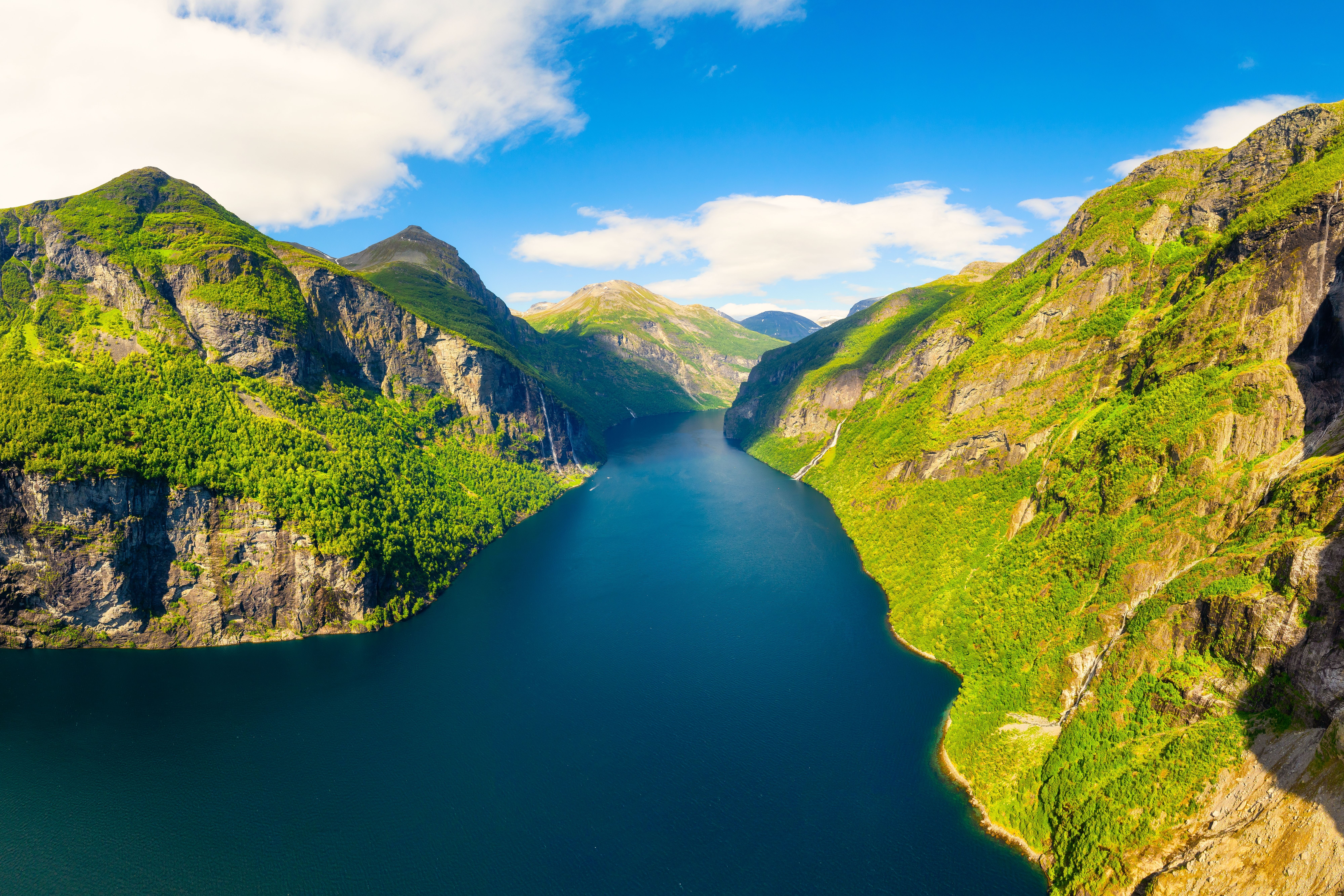 Aerial view of Geiranger Fjord, Norway, with deep blue waters surrounded by lush green cliffs and rugged mountains.