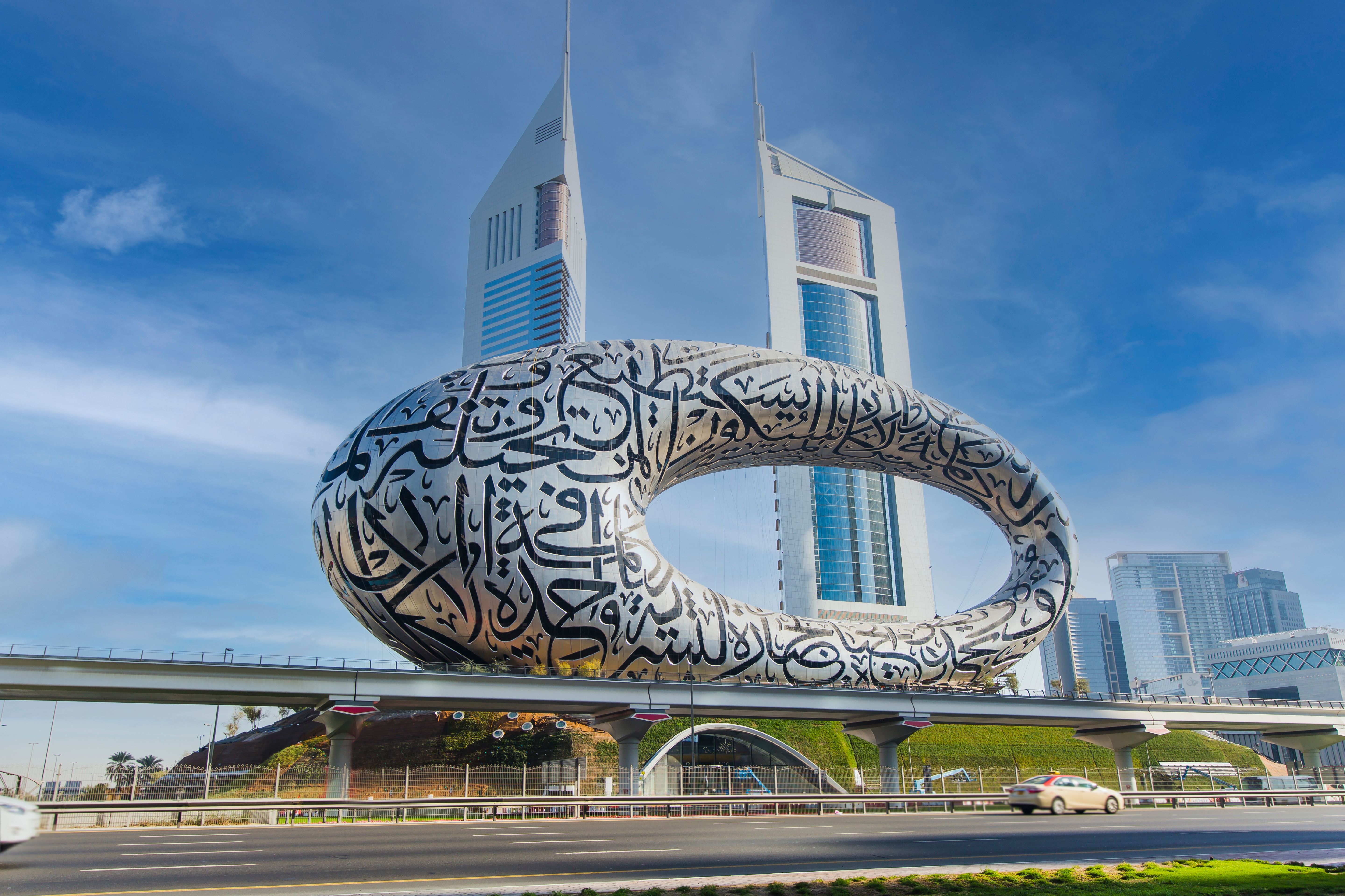Museum of the Future in Dubai with Arabic calligraphy, set against the Emirates Towers and a clear blue sky.