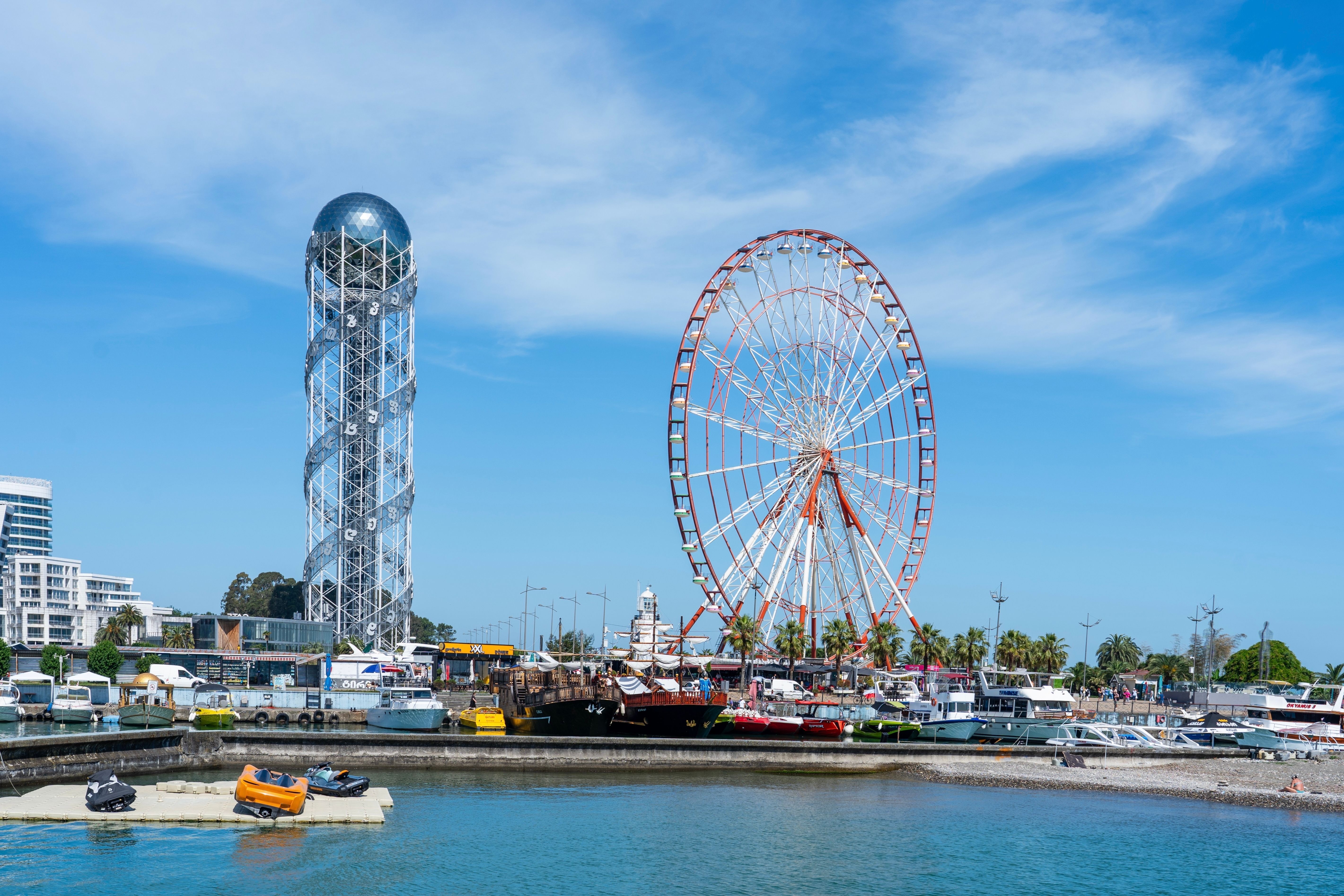 Batumi, Georgia waterfront with the Alphabet Tower, Ferris wheel, and boats docked in the harbor under a clear blue sky.
